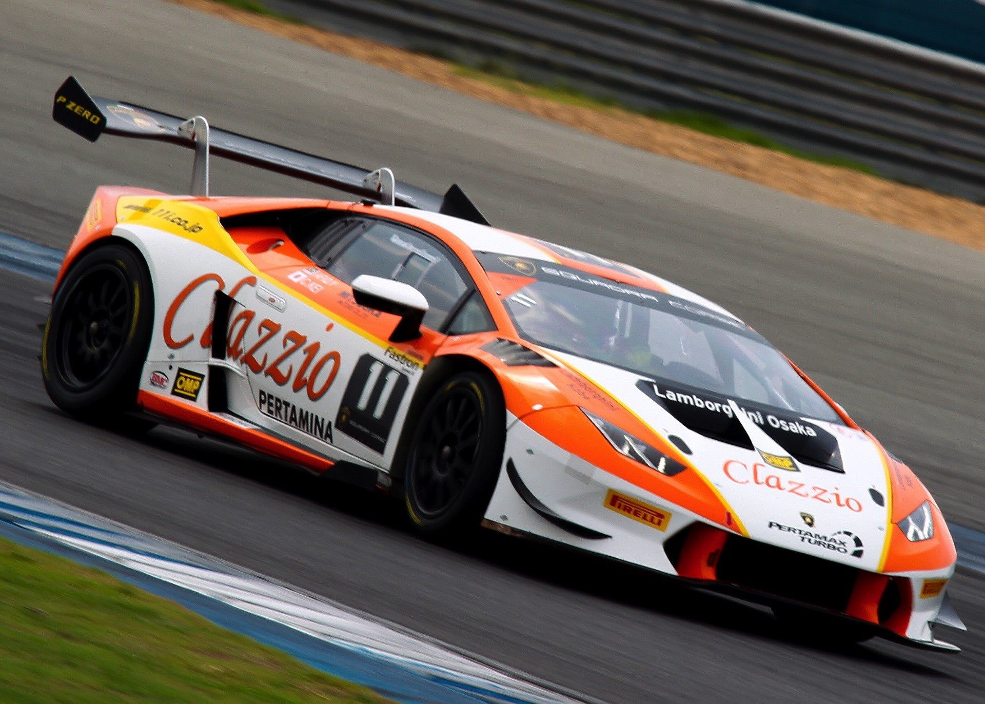 White and orange Lamborghini Huracán Super Trofeo race car at speed on a circuit, with large rear wing and Pirelli P Zero tires visible
