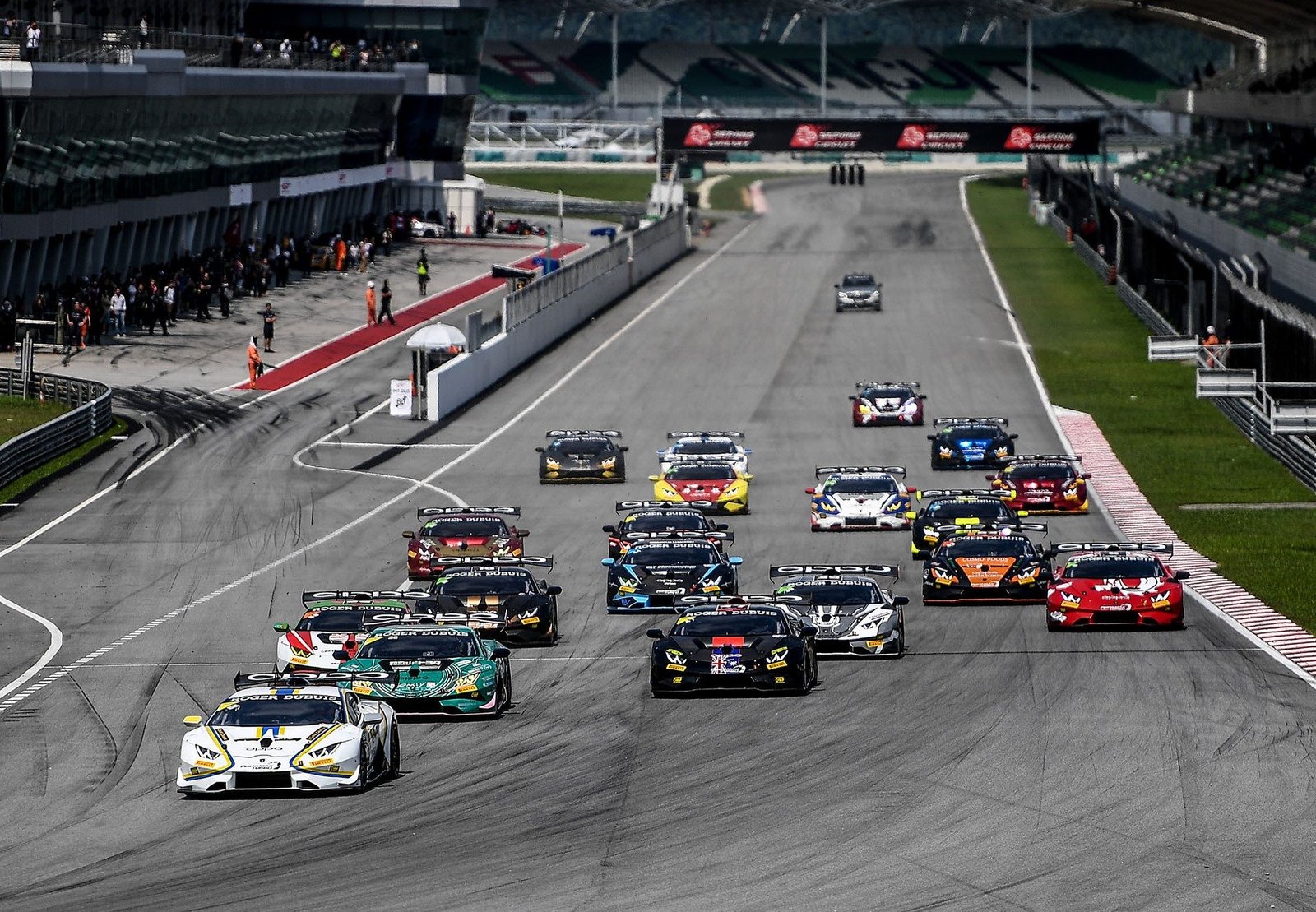 Multiple Lamborghini Huracán Super Trofeo race cars competing closely on track with spectators in the grandstands
