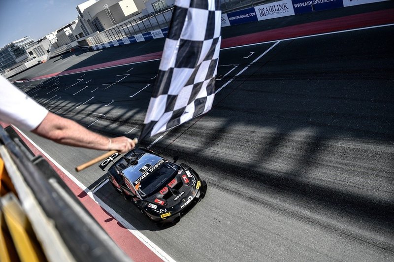 Black Lamborghini Huracán Super Trofeo Evo crossing the finish line under the checkered flag at the Dubai Autodrome