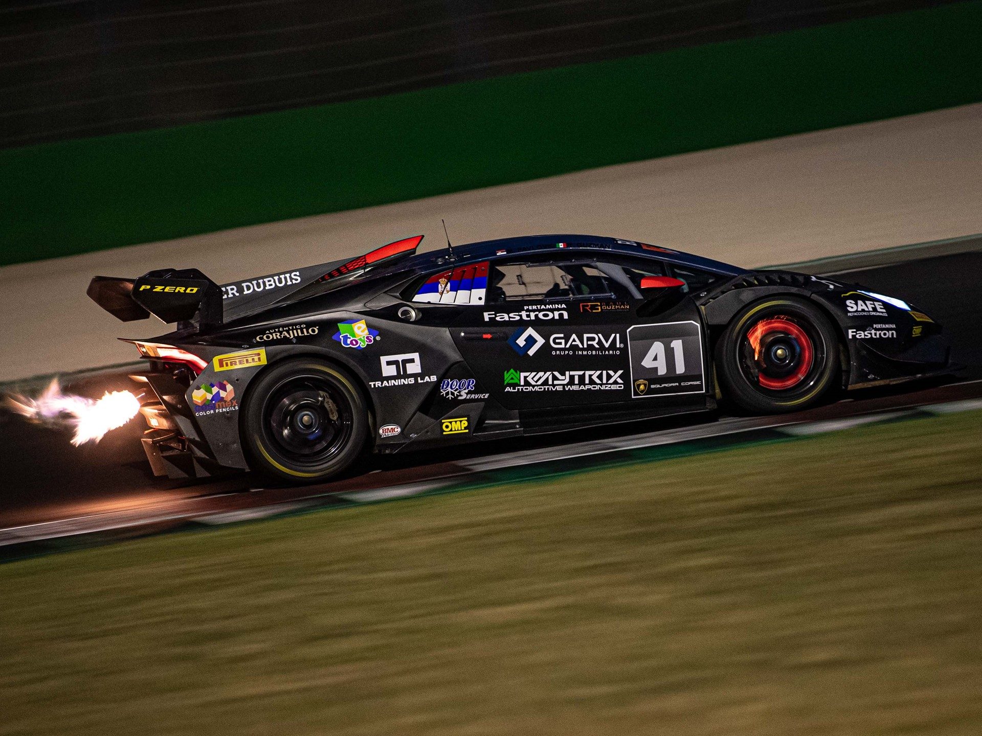 Black Lamborghini Huracán Super Trofeo EVO race car number 41 on track at night with exhaust flames and glowing brake discs