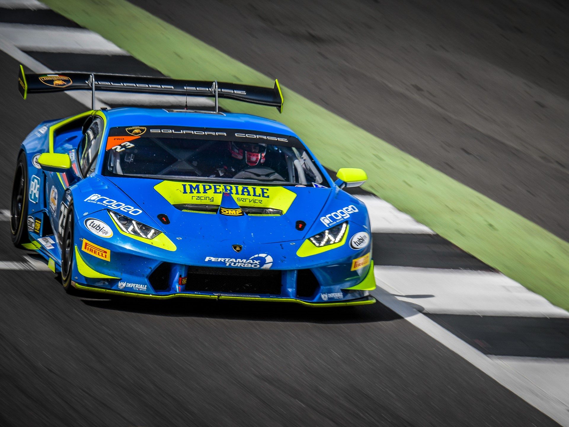 A blue and yellow Lamborghini Huracán Super Trofeo race car at speed on track, showing its large rear wing and aerodynamic body kit