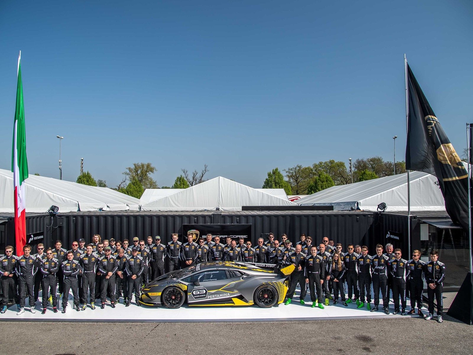 Lamborghini Squadra Corse team gathered around a grey and yellow Huracán Super Trofeo EVO race car bearing the number 63