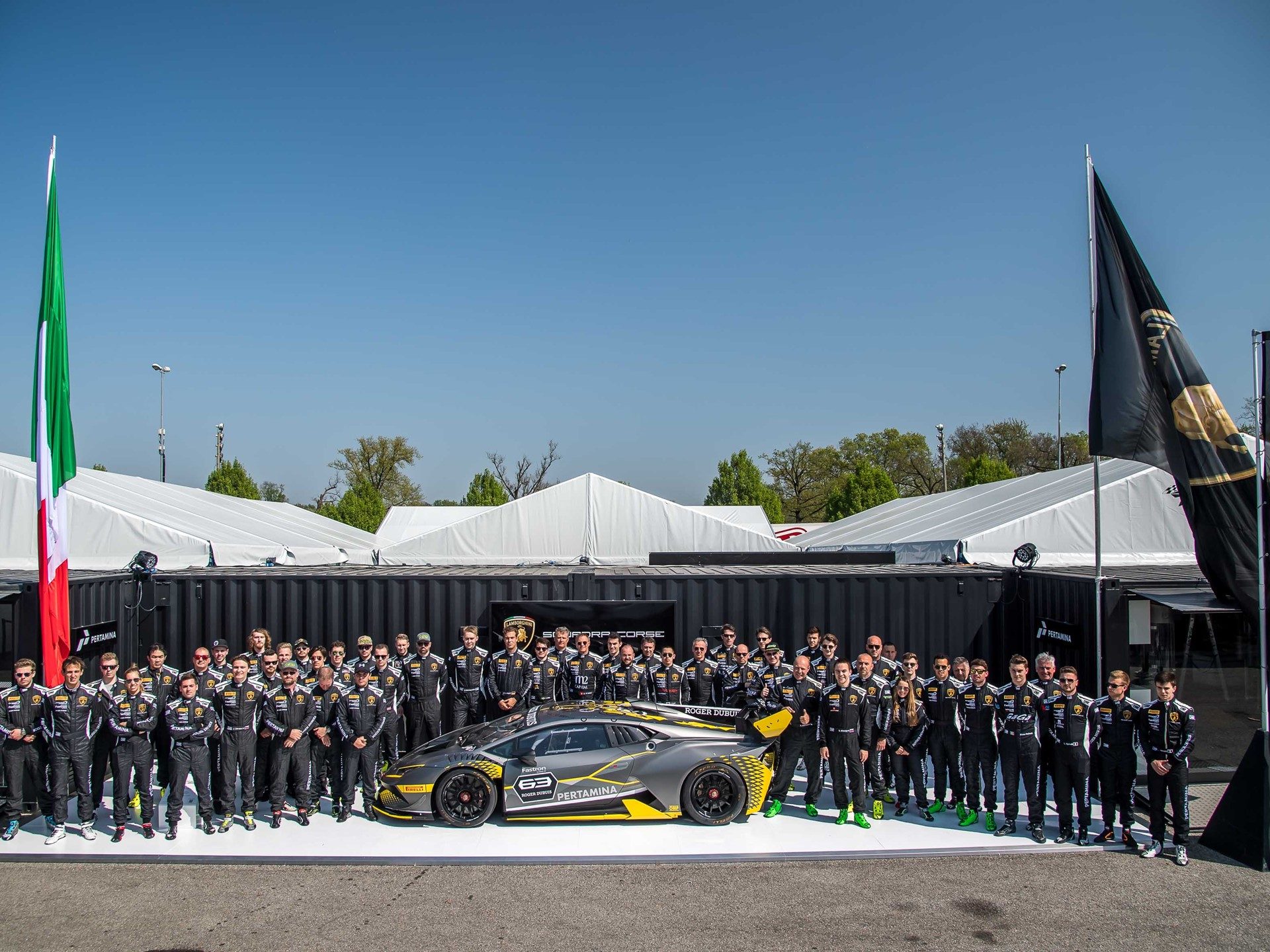 Lamborghini squadra corse team gathered around a grey and yellow huracán super trofeo evo race car bearing the number 63