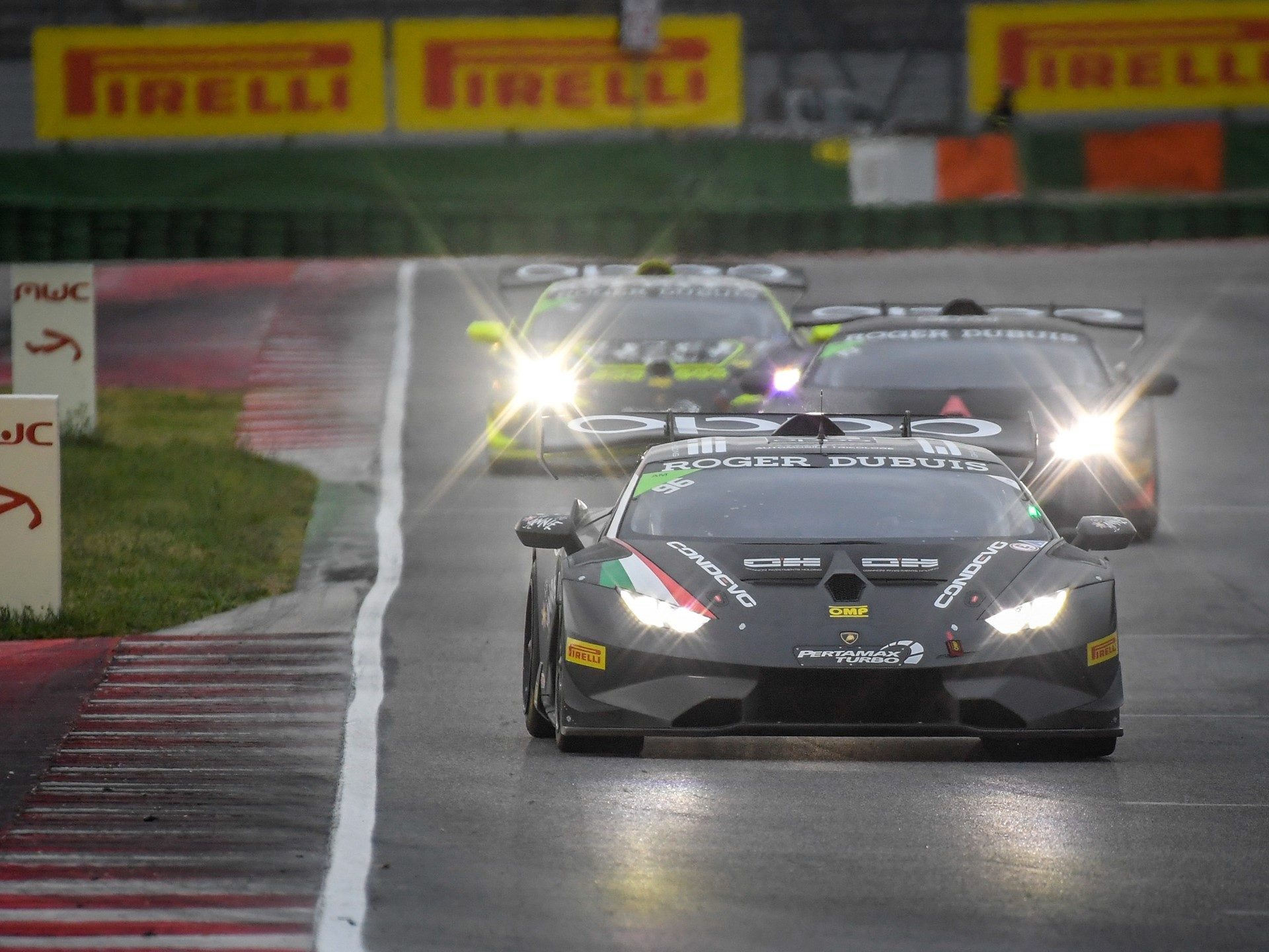 Lamborghini Huracán Super Trofeo EVO race cars battling on a wet circuit with headlights illuminated