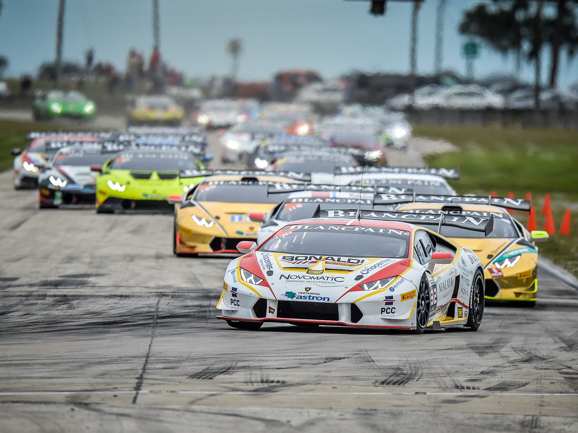 Lamborghini Huracán Super Trofeo race cars in close formation on track, showing aerodynamic body kits and large rear wings