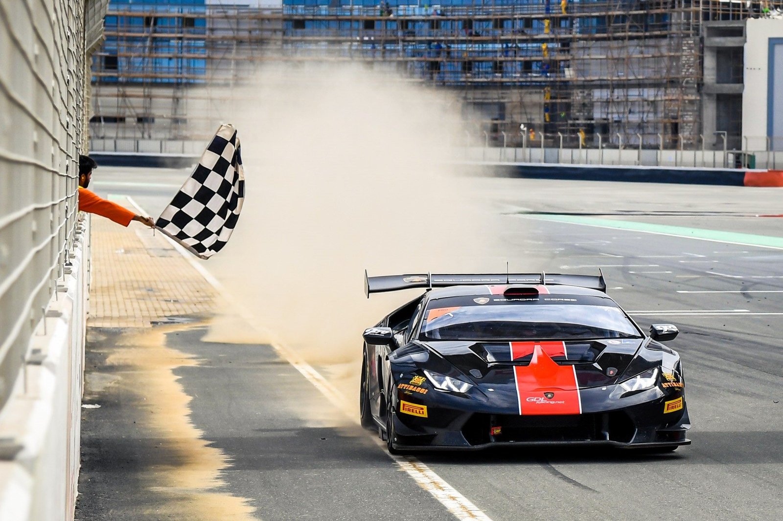 A black Lamborghini Huracán Super Trofeo race car with red accents crosses the finish line under a checkered flag at the Dubai Autodrome