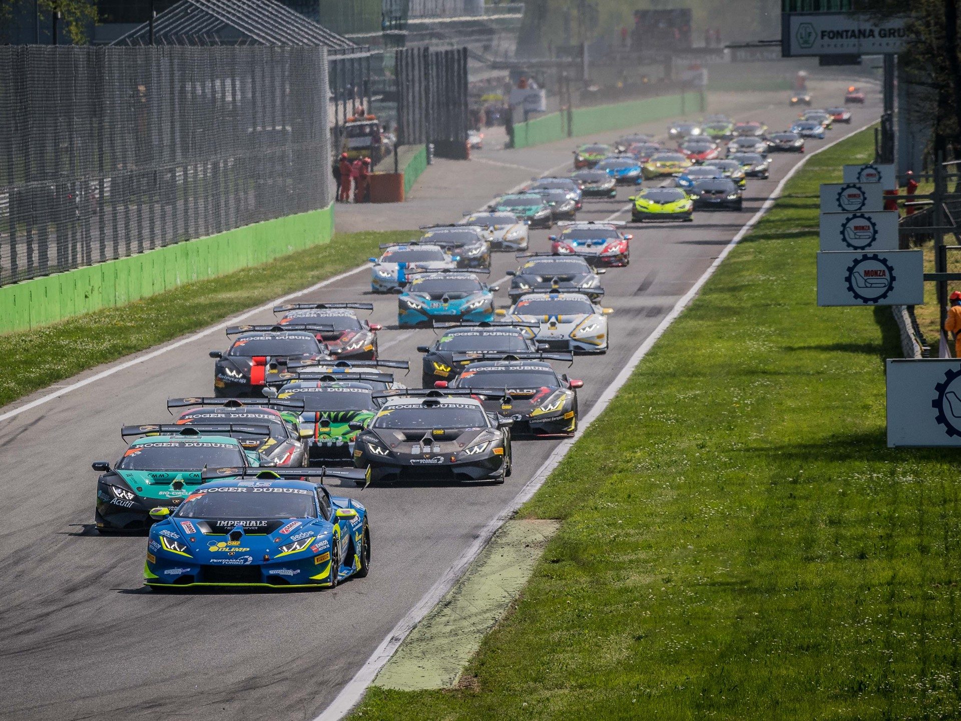 A fleet of Lamborghini Huracán Super Trofeo race cars in various liveries battling through a corner at Monza during the 2018 season opener