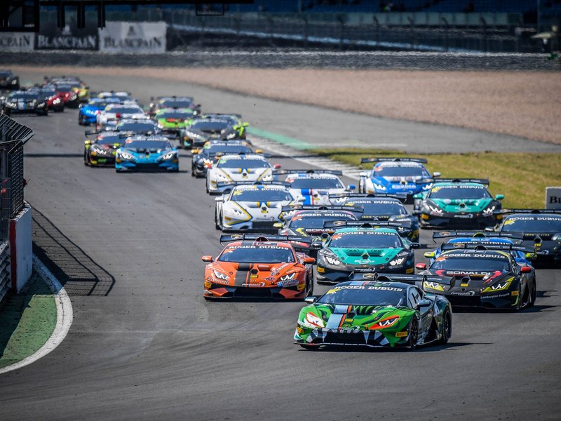 A pack of Lamborghini Huracán Super Trofeo race cars battle for position on a racetrack, led by a green and black liveried car