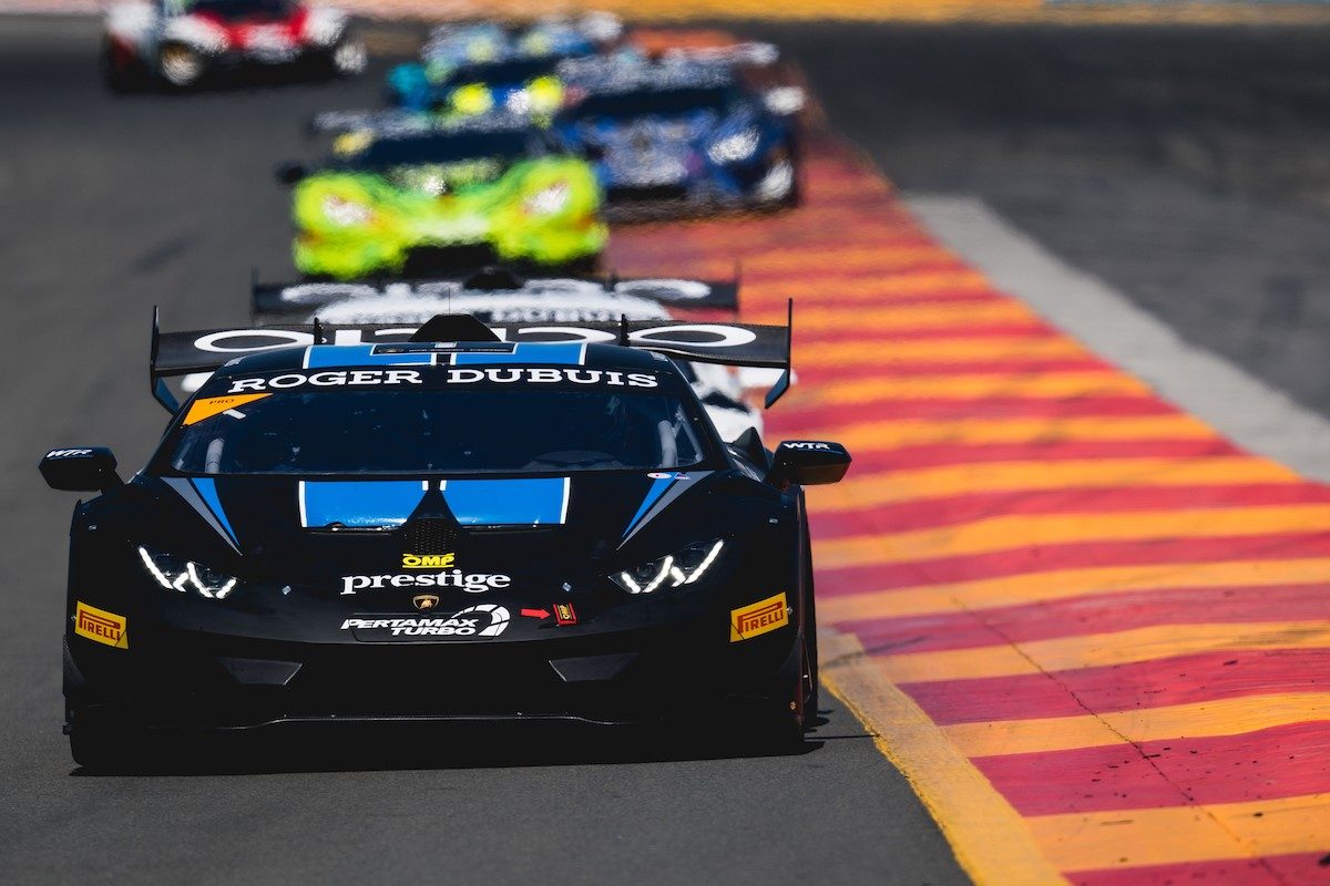 A black Lamborghini Huracán Super Trofeo race car with blue accents leads a pack through a corner at Watkins Glen International