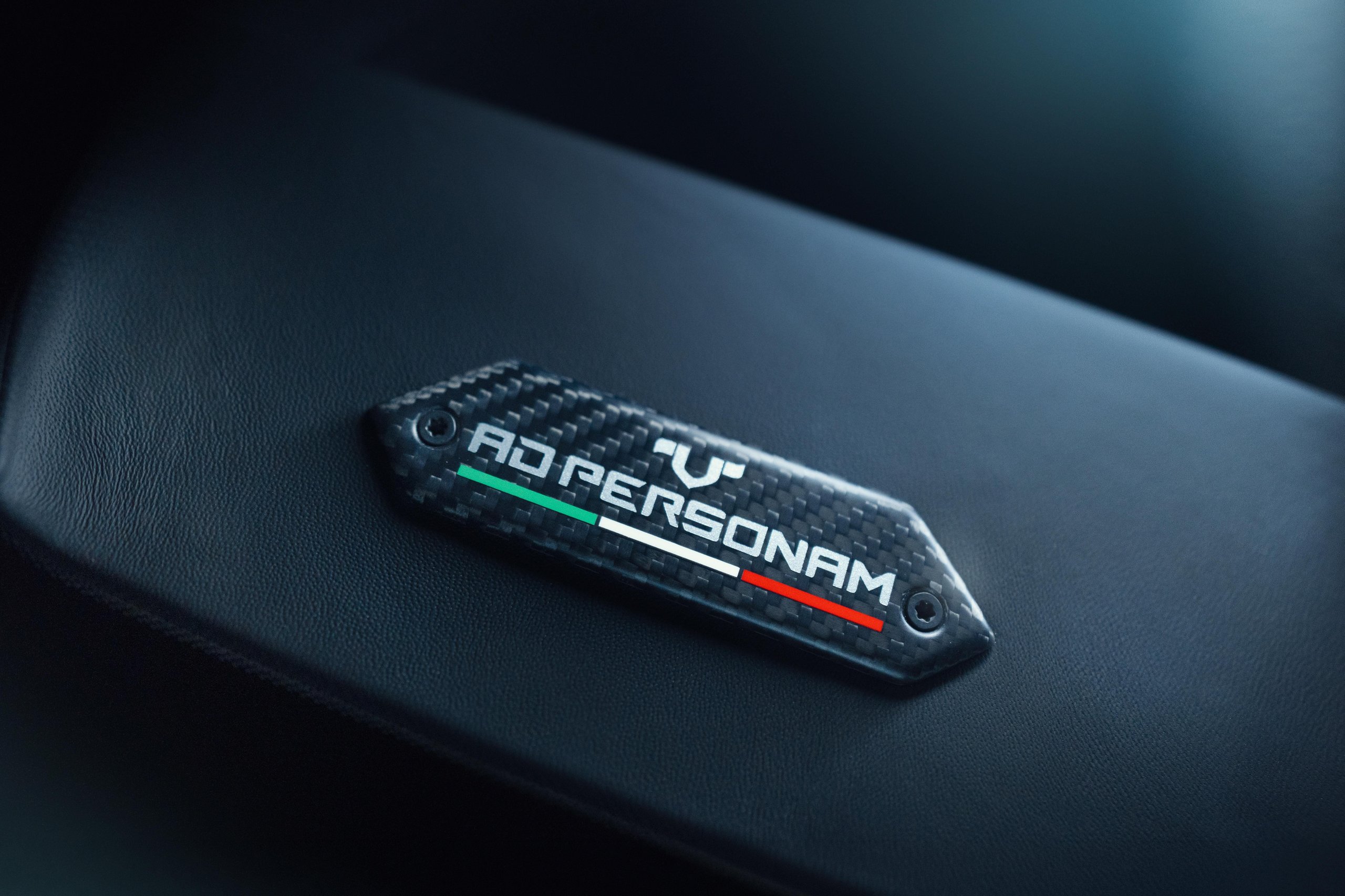 Close-up of the Ad Personam badge with Italian tricolore on carbon fiber interior surface