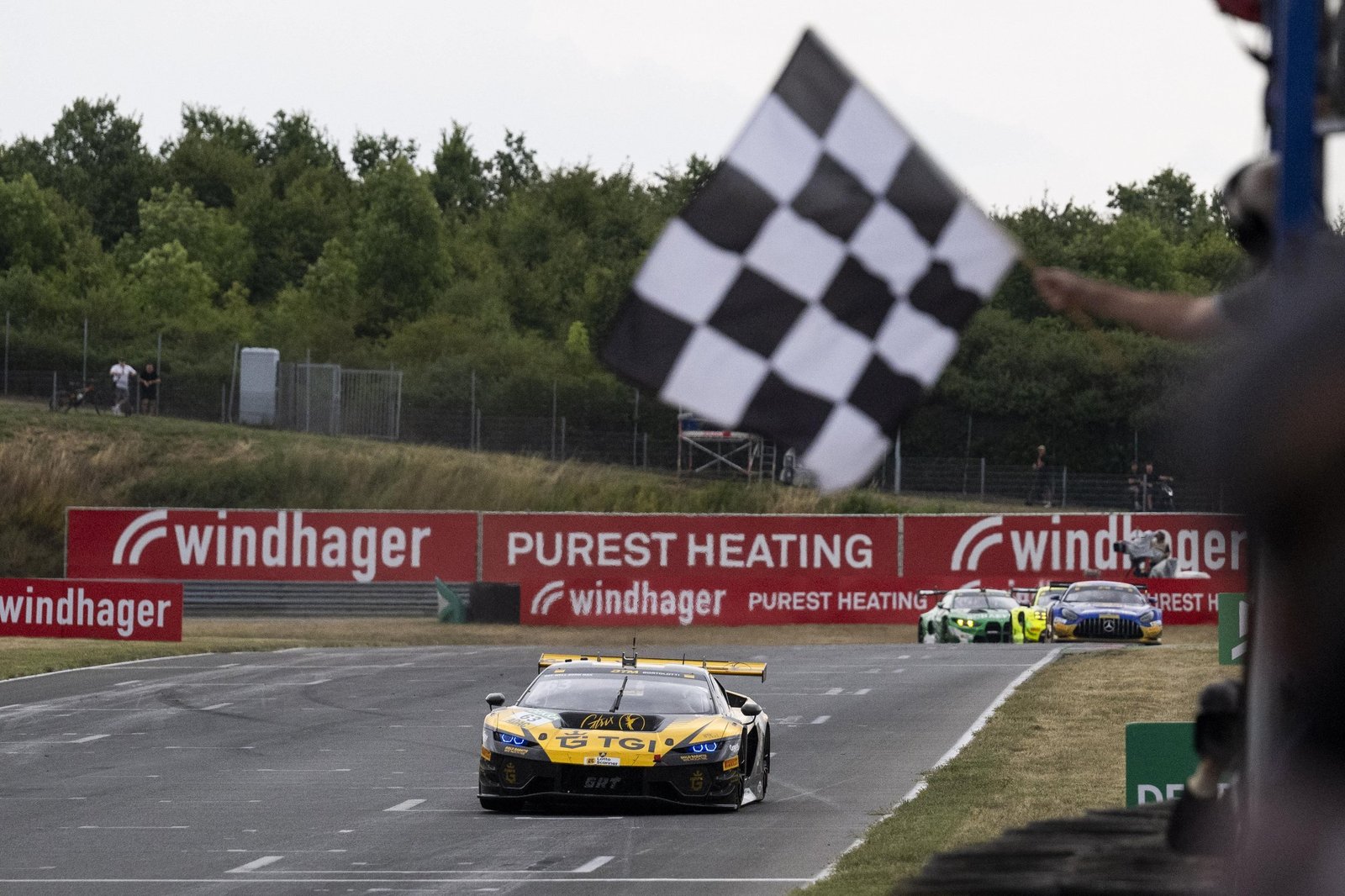 Yellow and black Lamborghini Temerario GT3 crosses the finish line under a checkered flag at Oschersleben DTM race