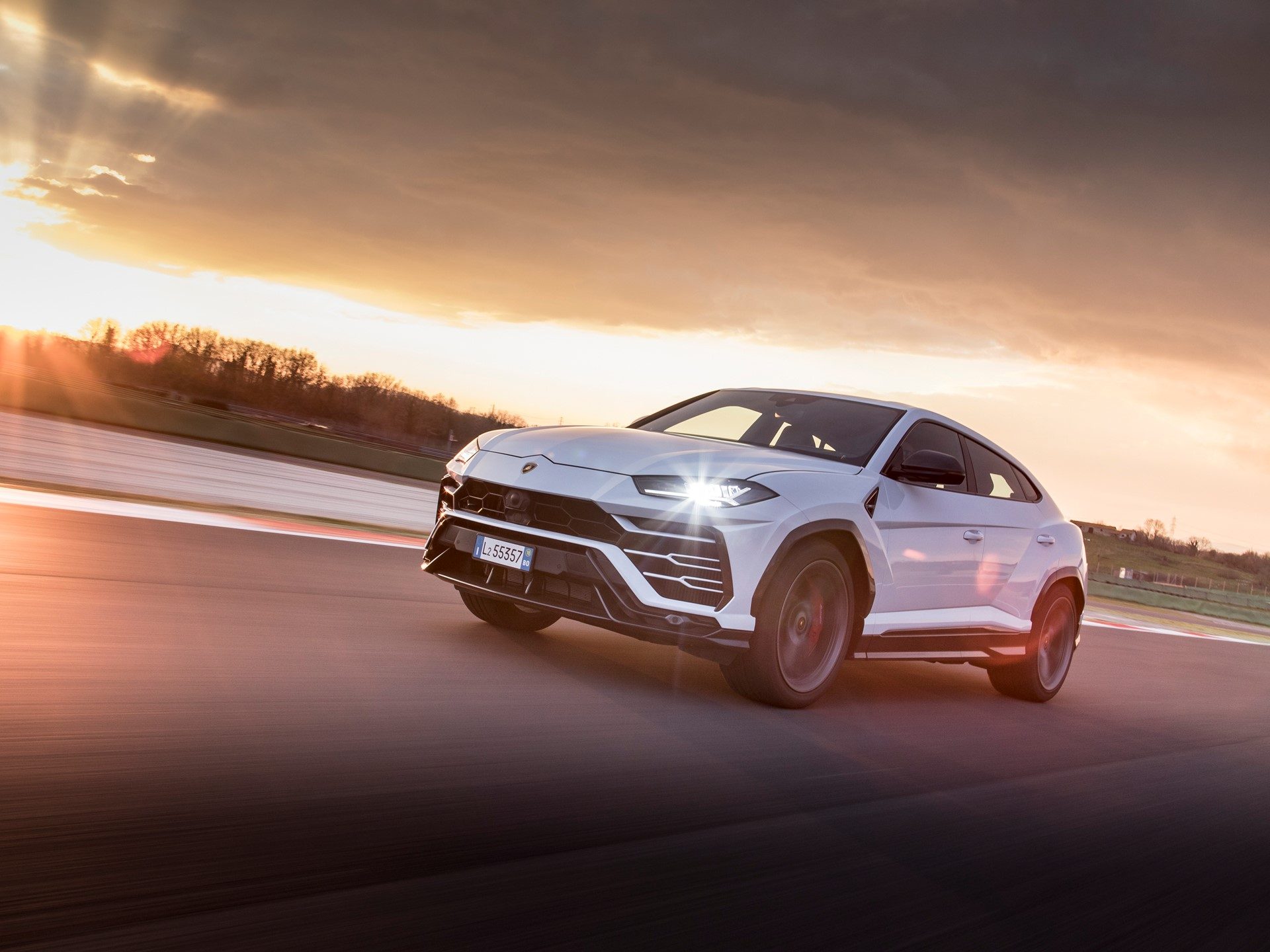 White Lamborghini Urus at speed on a track at sunset, showcasing its aggressive design and performance SUV capability