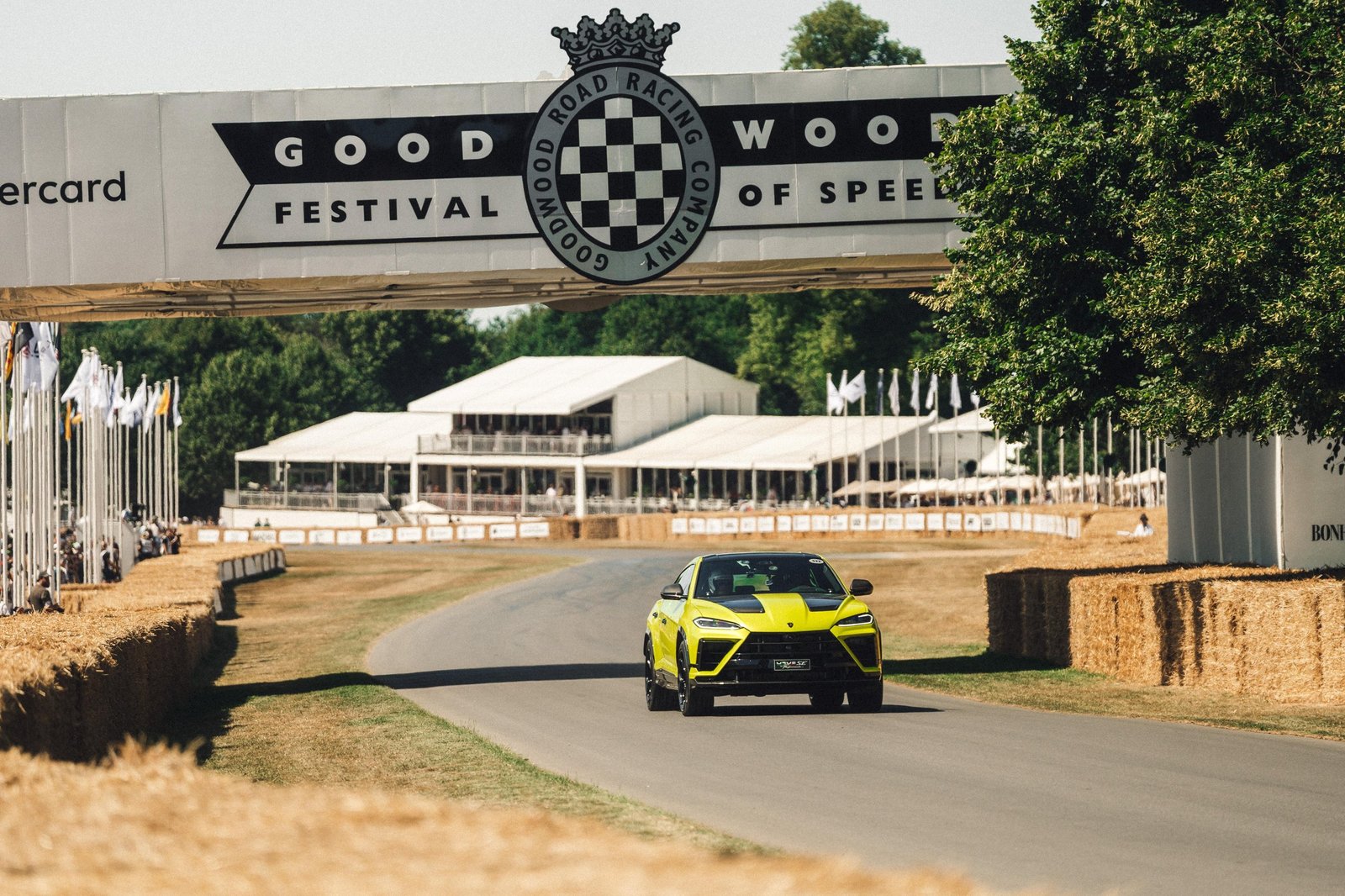Yellow Lamborghini Urus SE Performante driving under the Goodwood Festival of Speed bridge during the hill climb