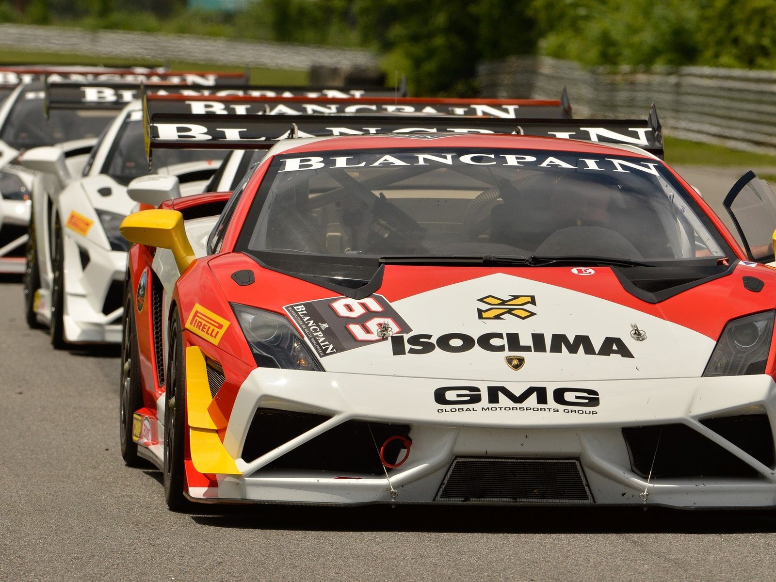 Red and white Lamborghini Gallardo Super Trofeo race car leading a pack of white Lamborghini race cars on track at the Blancpain Super Trofeo series