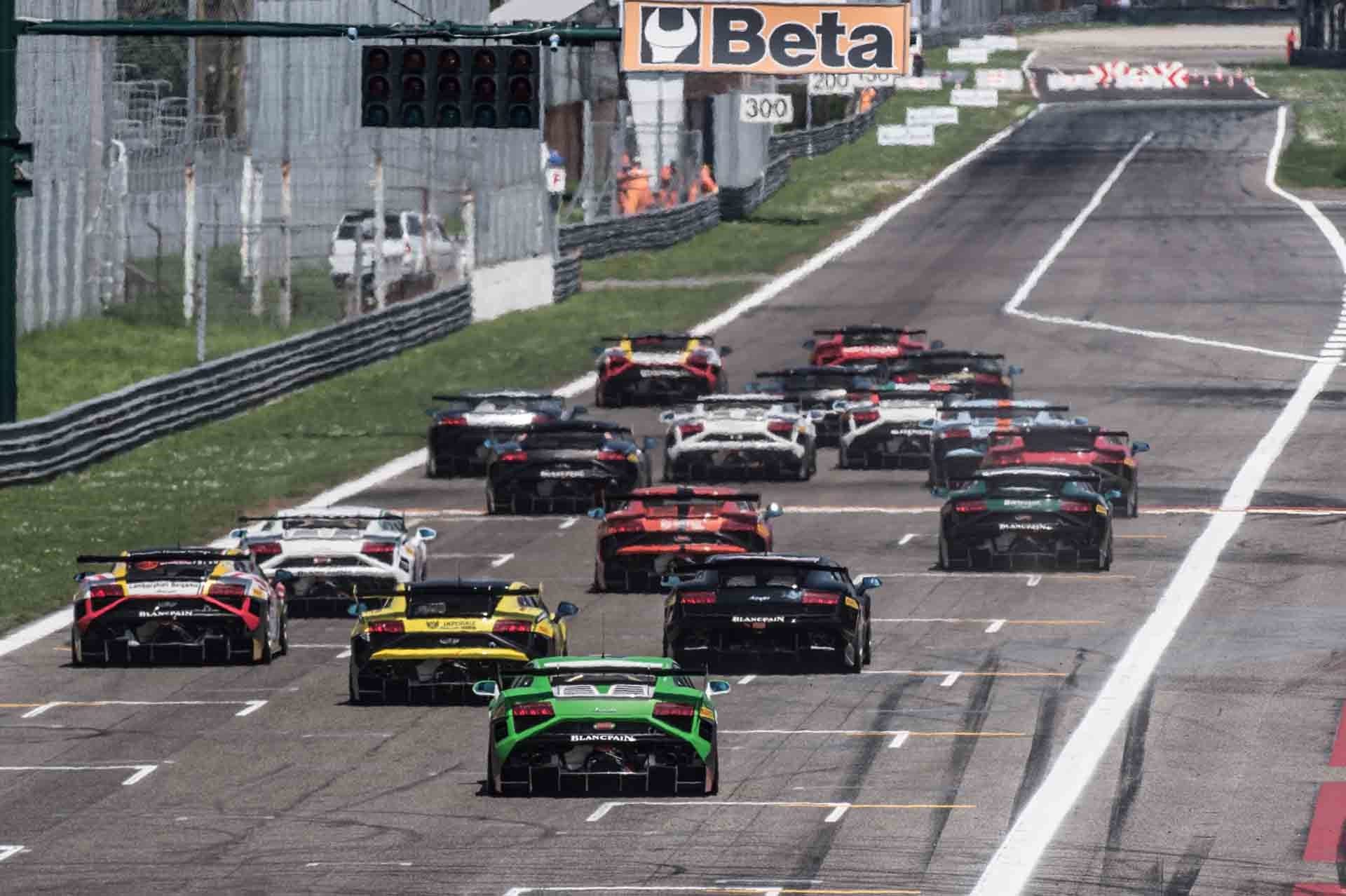Fleet of Lamborghini Gallardo LP 570-4 Super Trofeo race cars in green, yellow, black, white, and red liveries lined up on a racetrack at the start of a race