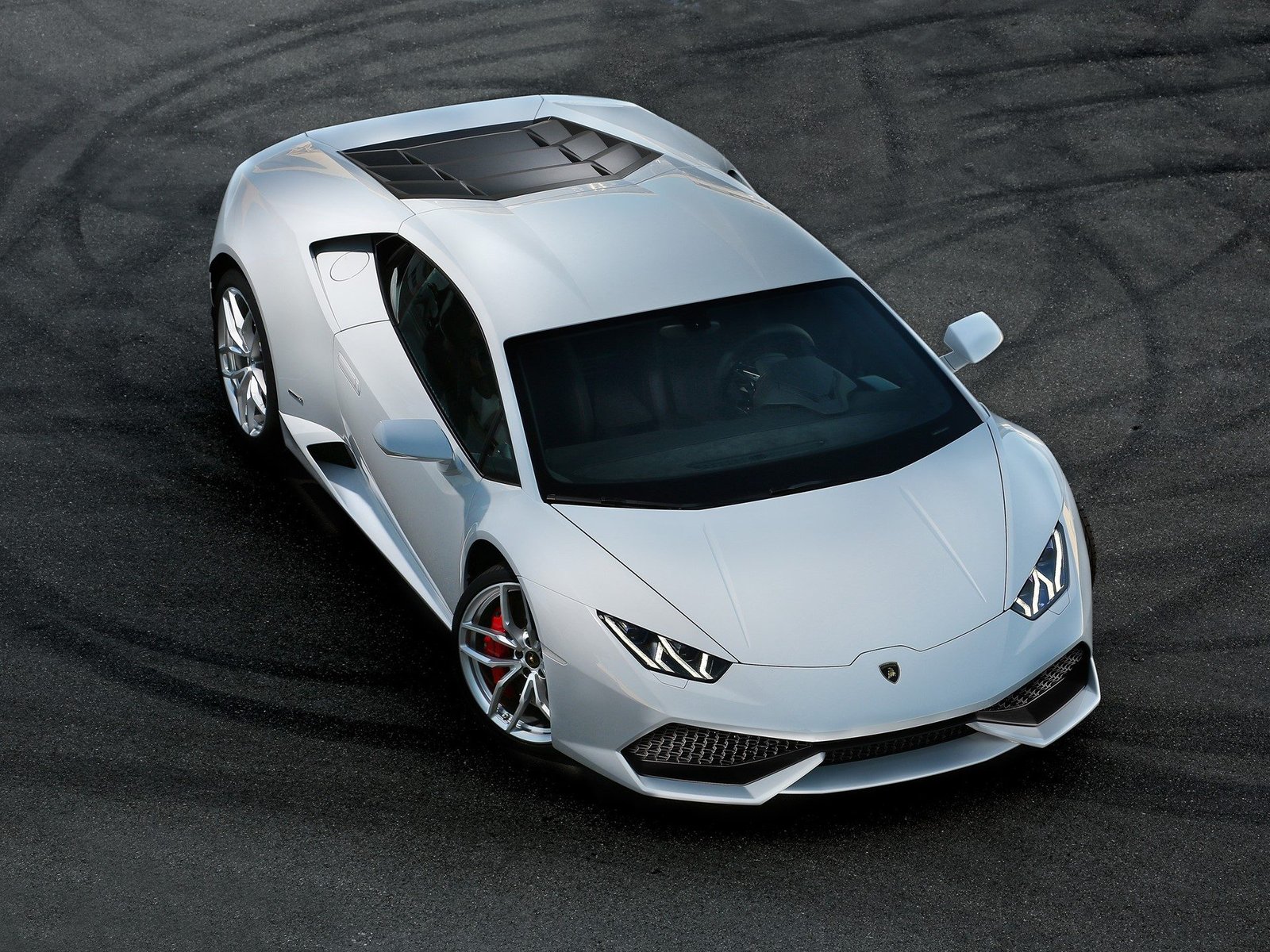White Lamborghini Huracán LP 610-4 photographed from above on dark asphalt, showing its sharp front fascia, Y-shaped LED running lights, and red brake calipers
