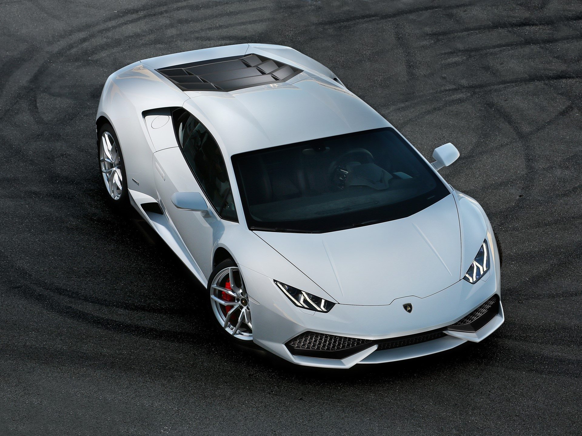 White Lamborghini Huracán LP 610-4 photographed from above on dark asphalt, showing its sharp front fascia, Y-shaped LED running lights, and red brake calipers