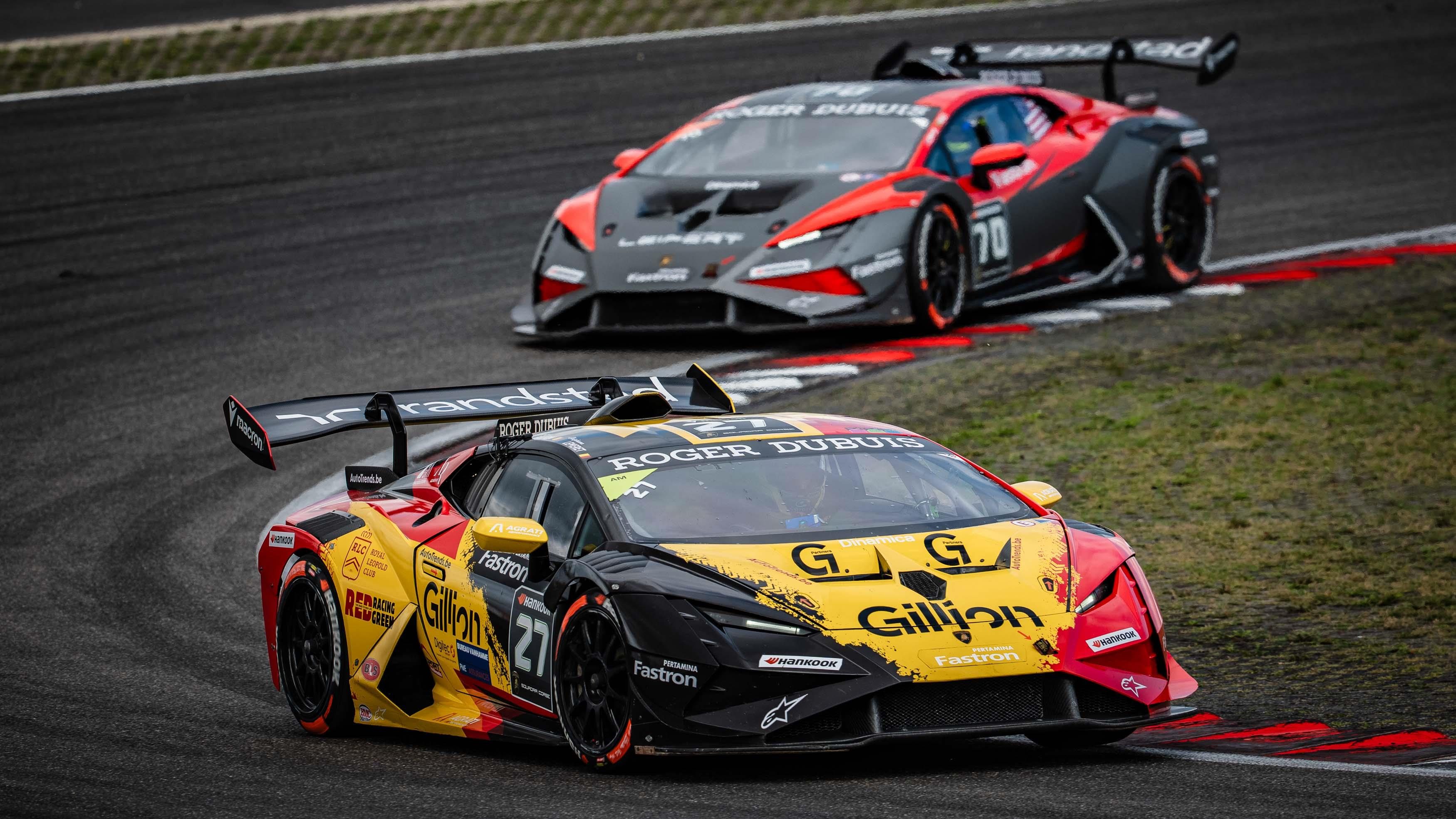 A multi-colored Lamborghini Huracán Super Trofeo EVO2 race car leads a grey and red Lamborghini Huracán Super Trofeo EVO2 on a racetrack.
