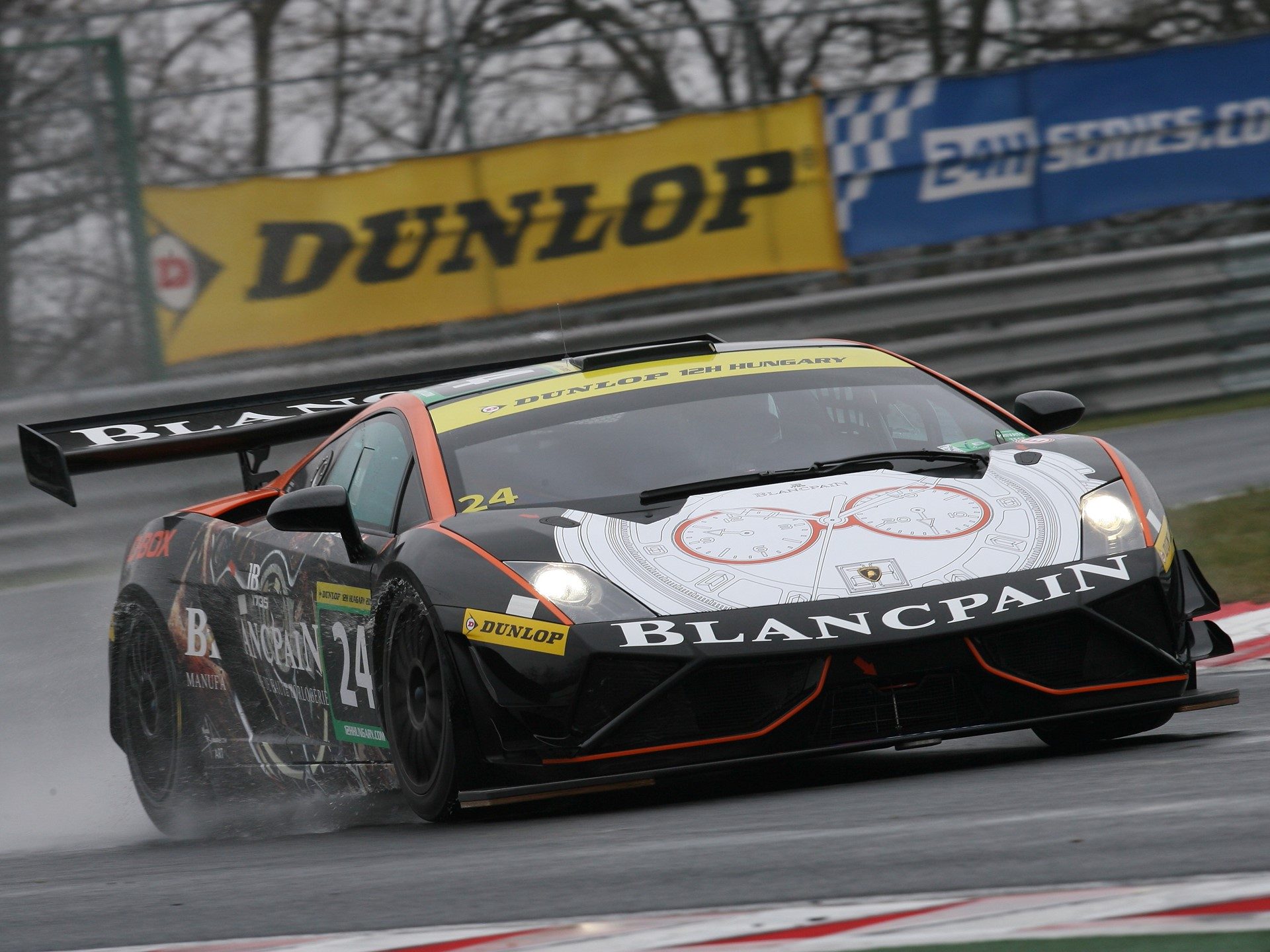 Black Lamborghini Gallardo GT3 FL2 race car with orange accents and Blancpain sponsorship racing through a wet track