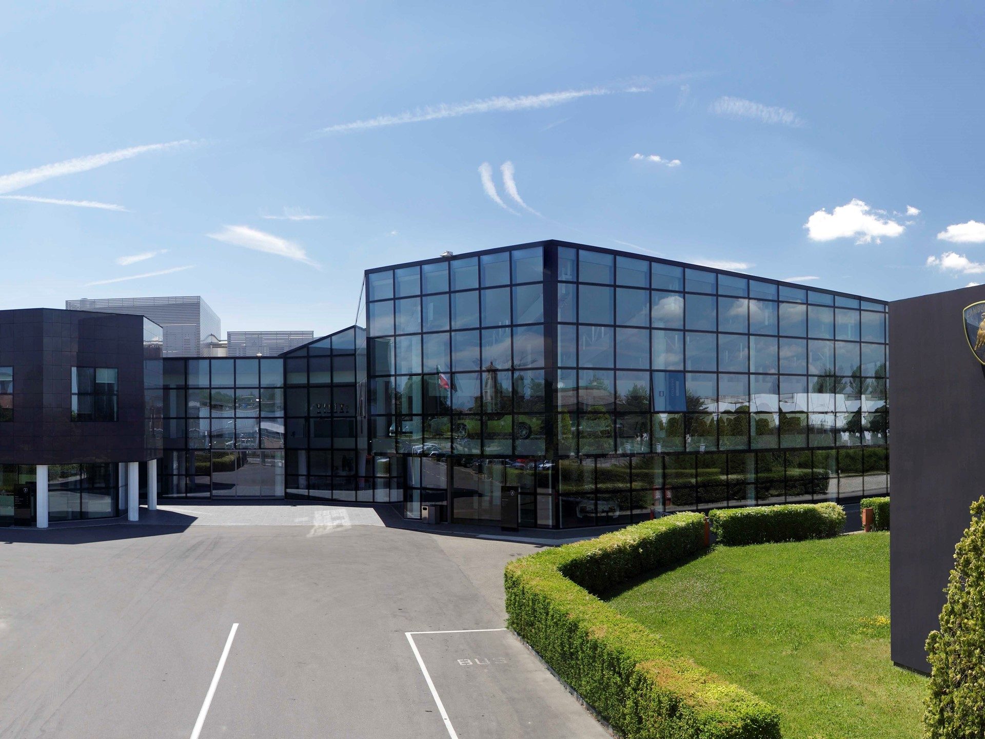 Exterior view of the Lamborghini factory in Sant'Agata Bolognese with its modern glass facade and the Lamborghini shield logo visible on the building