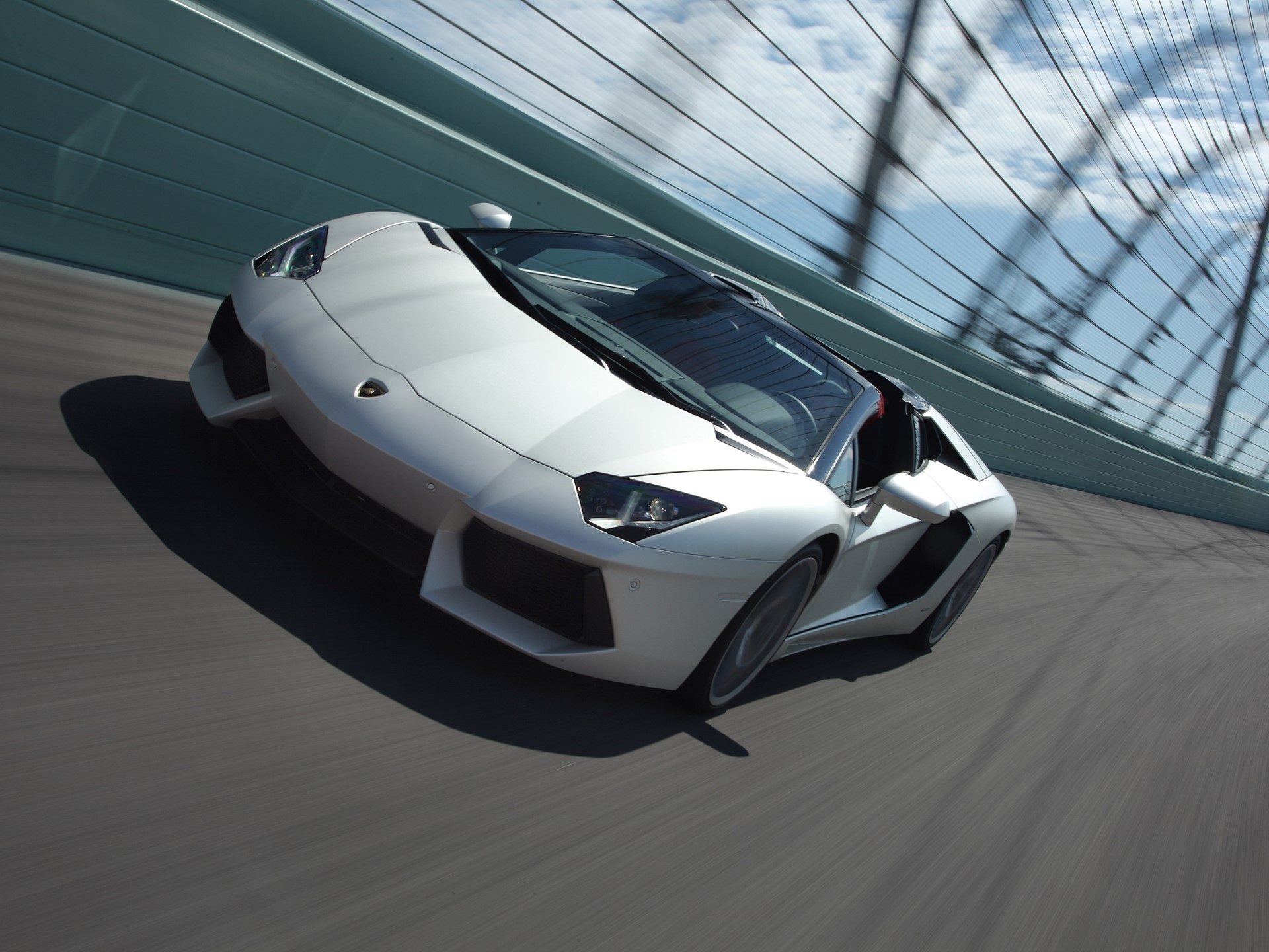 White Lamborghini Aventador Roadster at speed on a racetrack, captured from a low dynamic angle with motion blur