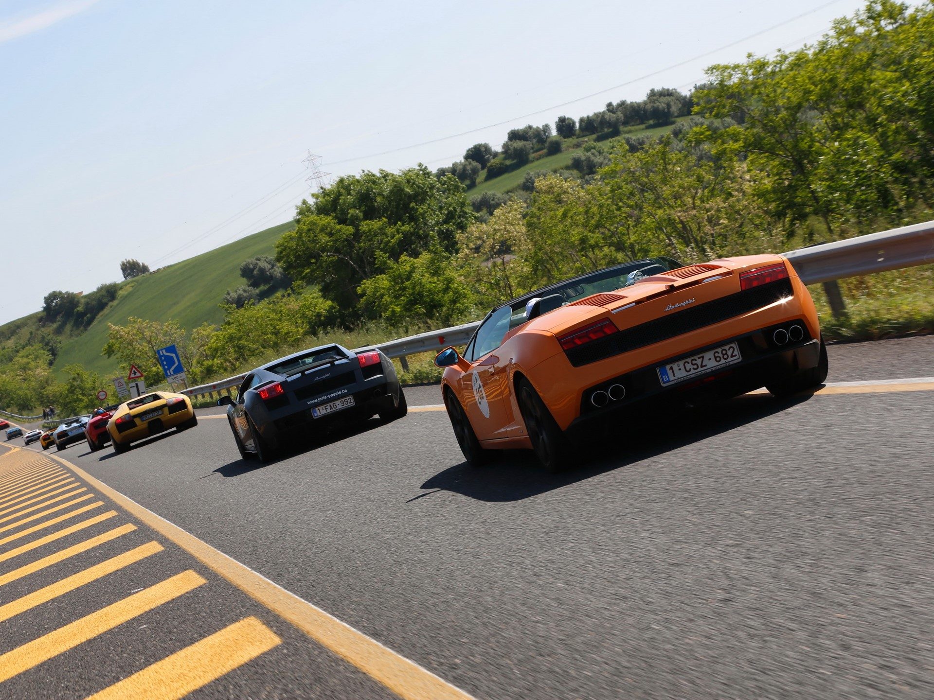 Lamborghini Gallardos in orange, black, and yellow navigating a winding Italian hillside road during the 50th Anniversary Grand Tour