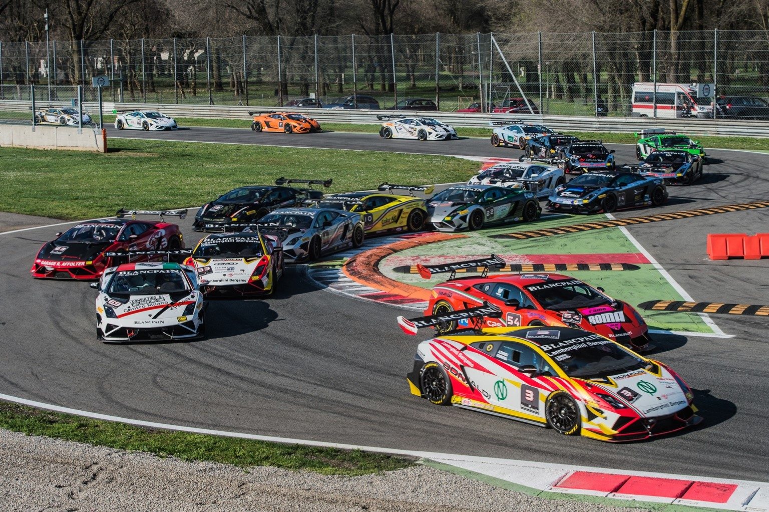 A pack of colorful Lamborghini Gallardo LP 570-4 Super Trofeo race cars battling through a corner on track, featuring prominent rear wings and racing liveries