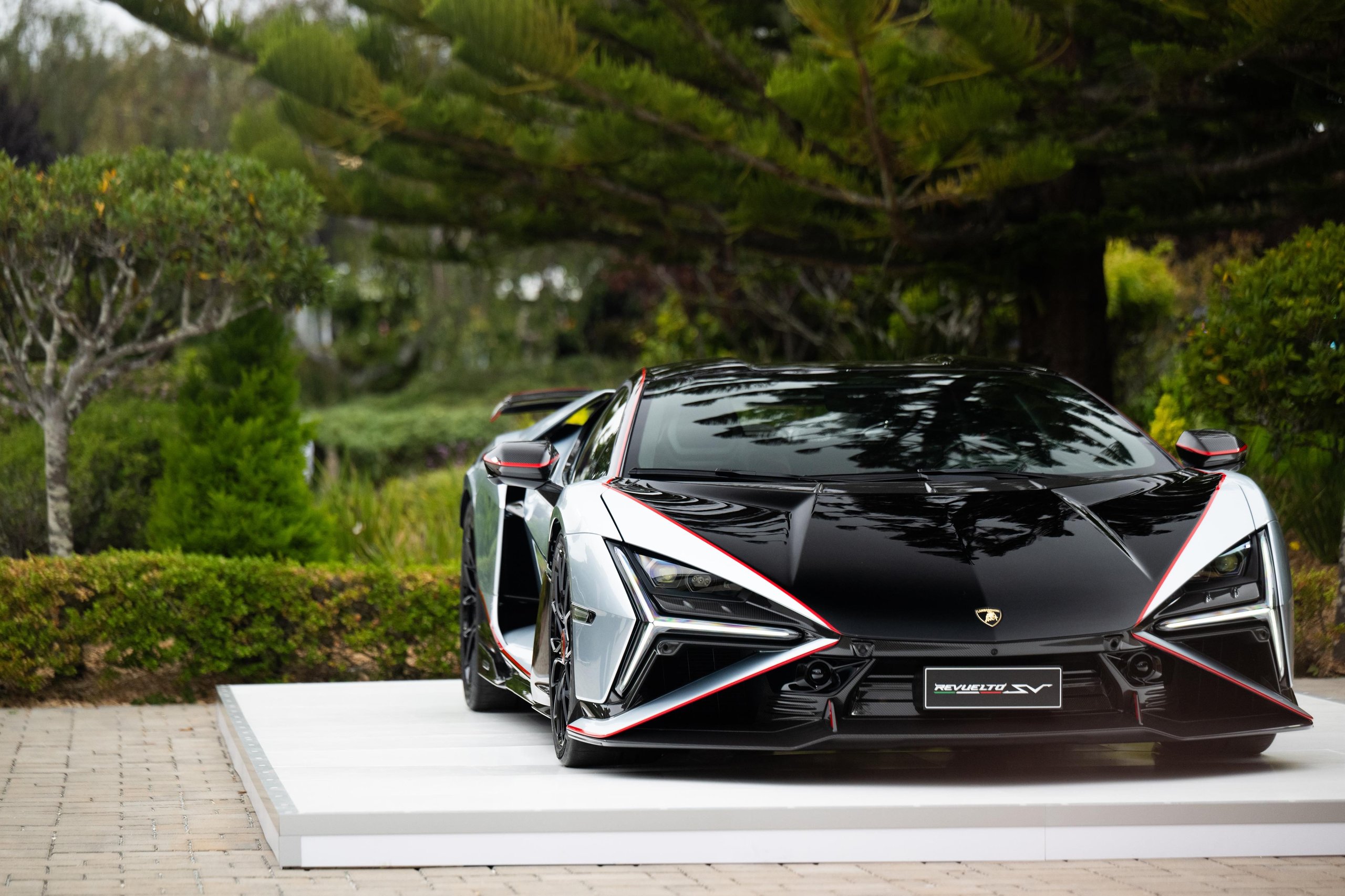 Black and white Lamborghini Revuelto SV with red accents on a white display platform at Monterey Car Week