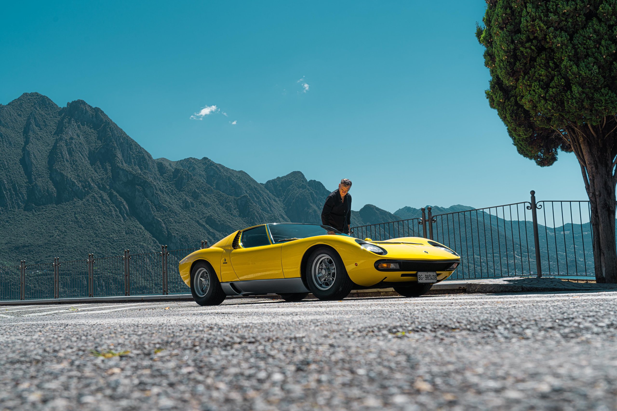 Lamborghini'S Miura Sv At 55: Why An Astronaut Behind The Wheel Says More Than Any Spec Sheet 11 Yellow lamborghini miura sv parked on a scenic road overlooking mountains and a lake with a figure standing behind