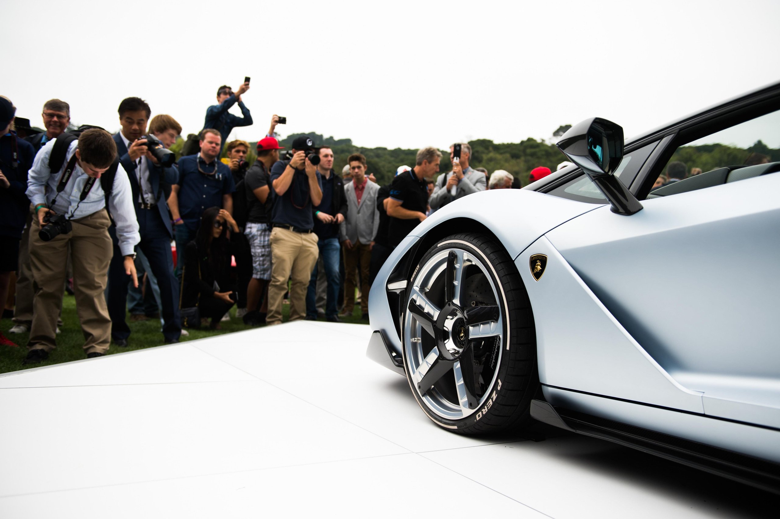Silver Lamborghini Centenario Roadster on display at an outdoor event with enthusiasts and photographers in the background