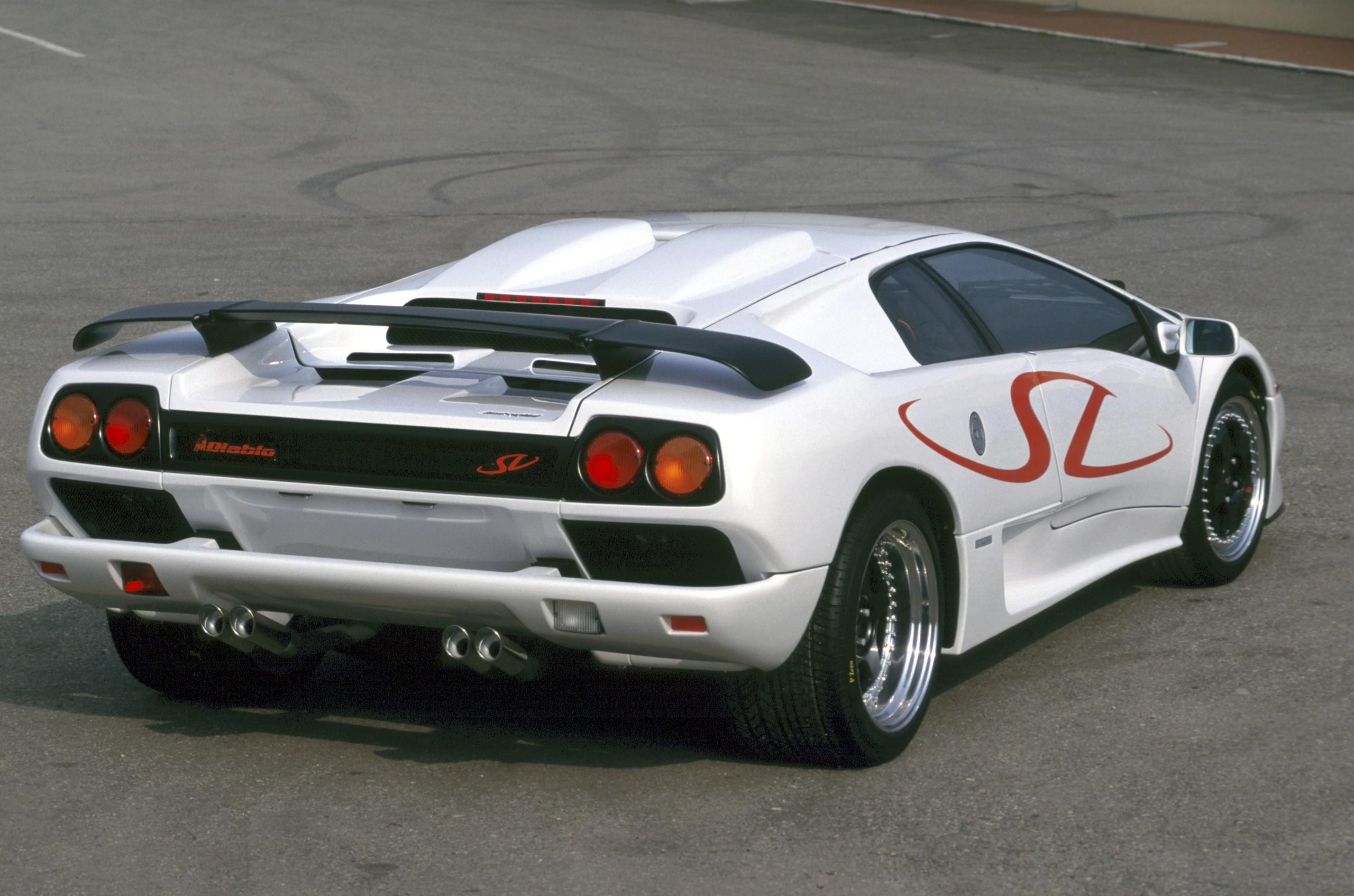 Rear-quarter view of a white Lamborghini Diablo SV with red SV decals, showing its iconic rear wing and taillights