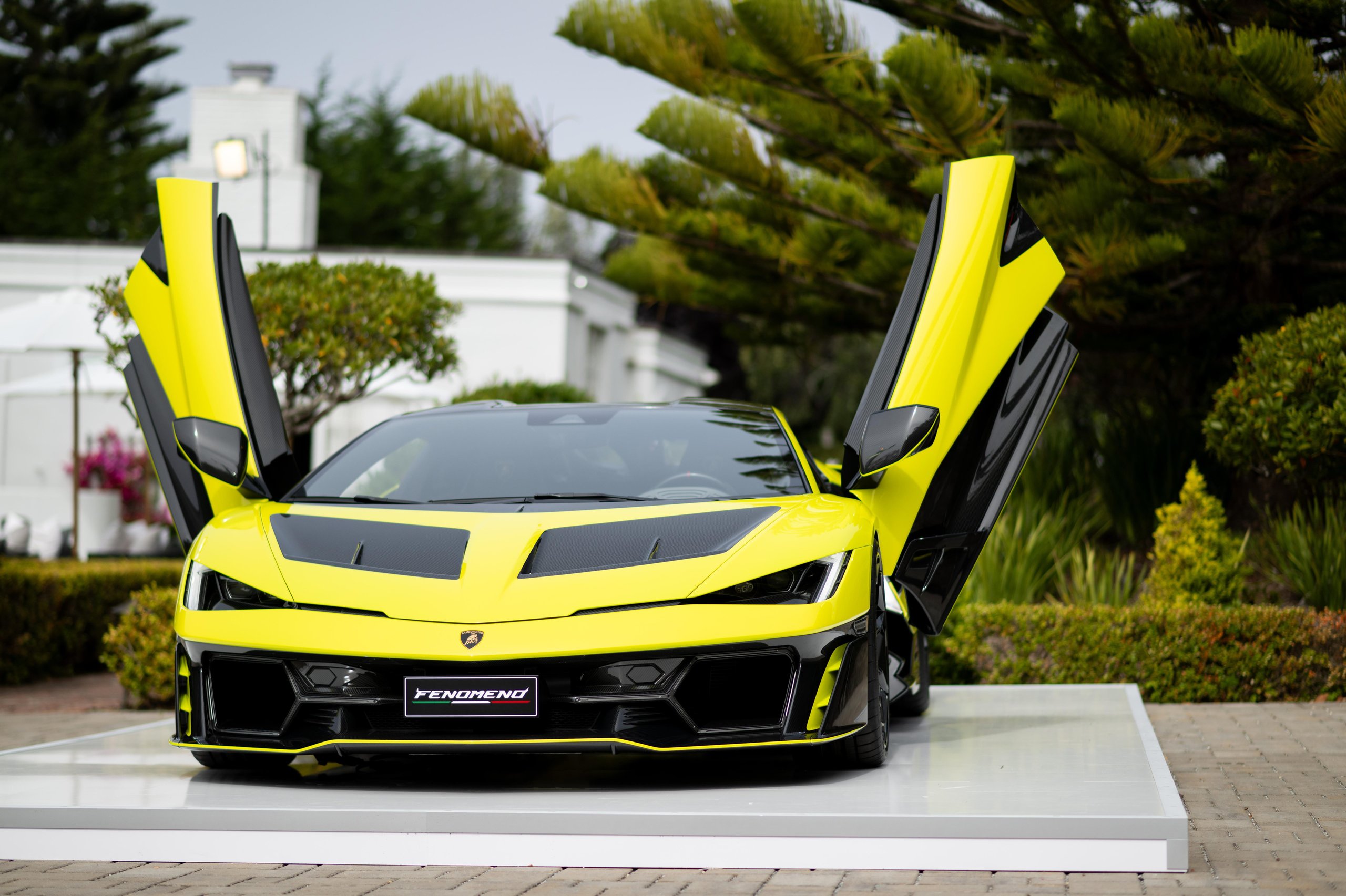 Yellow-and-black Lamborghini Fenomeno with its scissor doors open on a white display platform at Monterey Car Week 2025