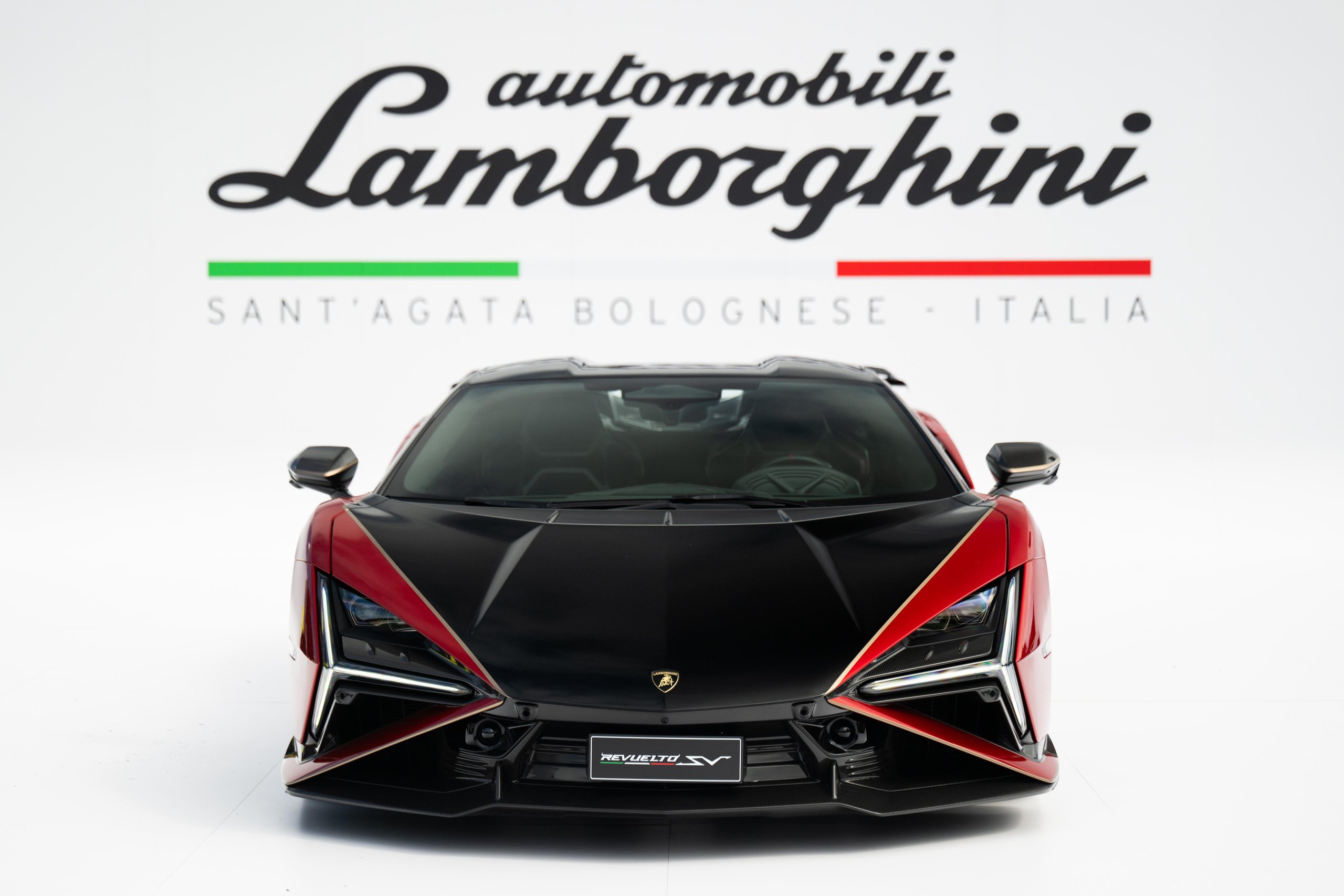 Head-on studio view of the black and red Lamborghini Revuelto SV against a white backdrop with Automobili Lamborghini branding