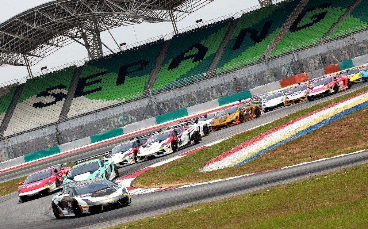 Lamborghini Gallardo Super Trofeo race cars in colorful liveries navigating a corner at Sepang International Circuit with grandstands in the background
