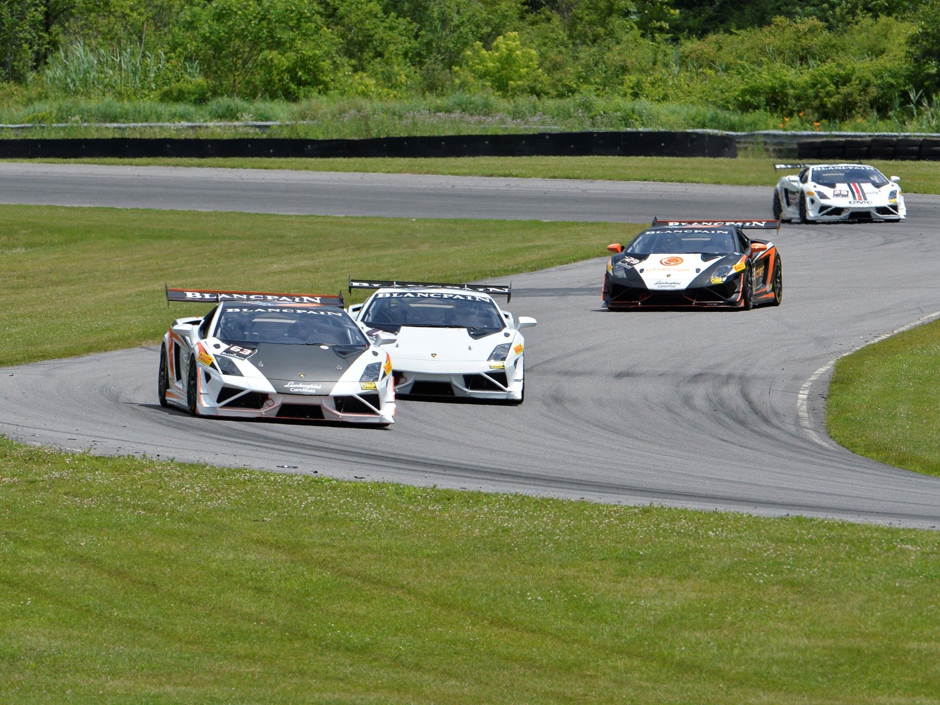Four Lamborghini Gallardo Super Trofeo race cars navigating a turn at Lime Rock Park with distinct racing liveries and large rear wings