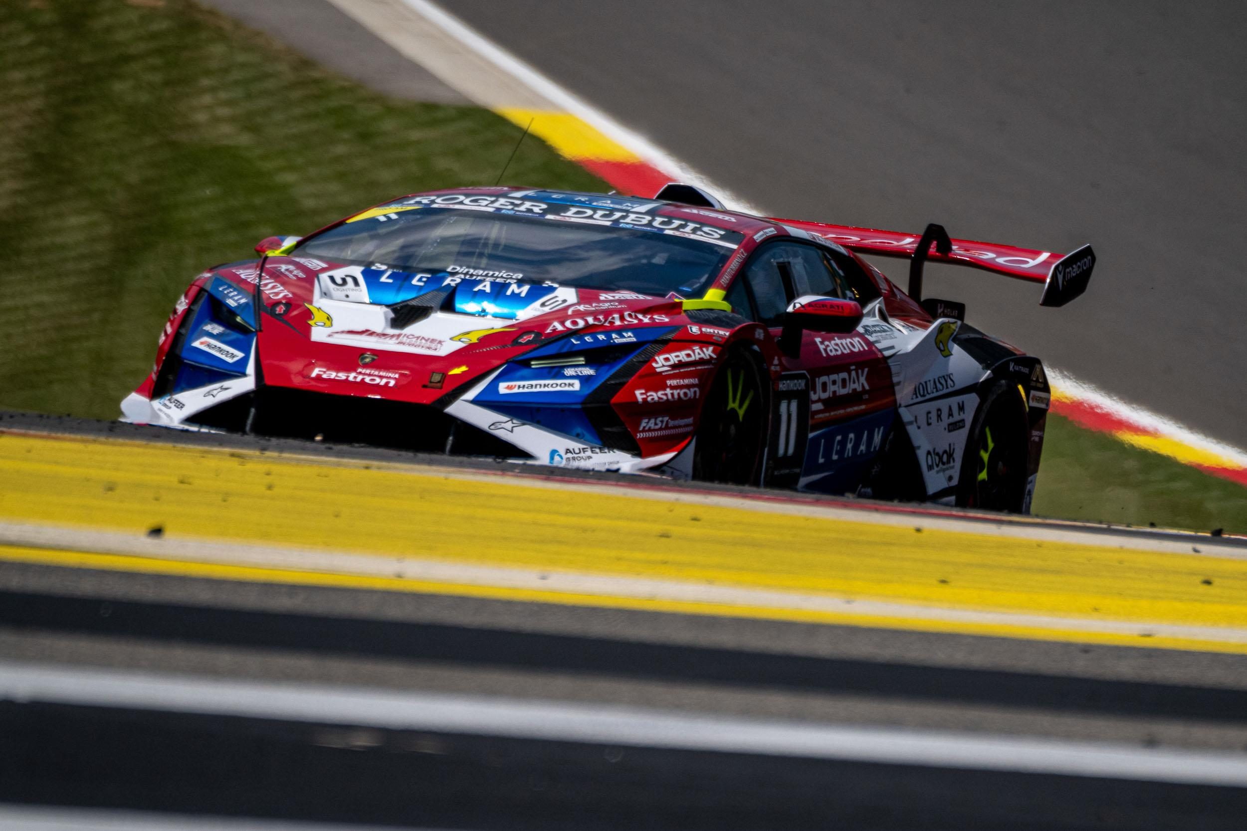A red, white, and blue Lamborghini Huracán Super Trofeo EVO2 race car number 11 leans into a turn on a racetrack