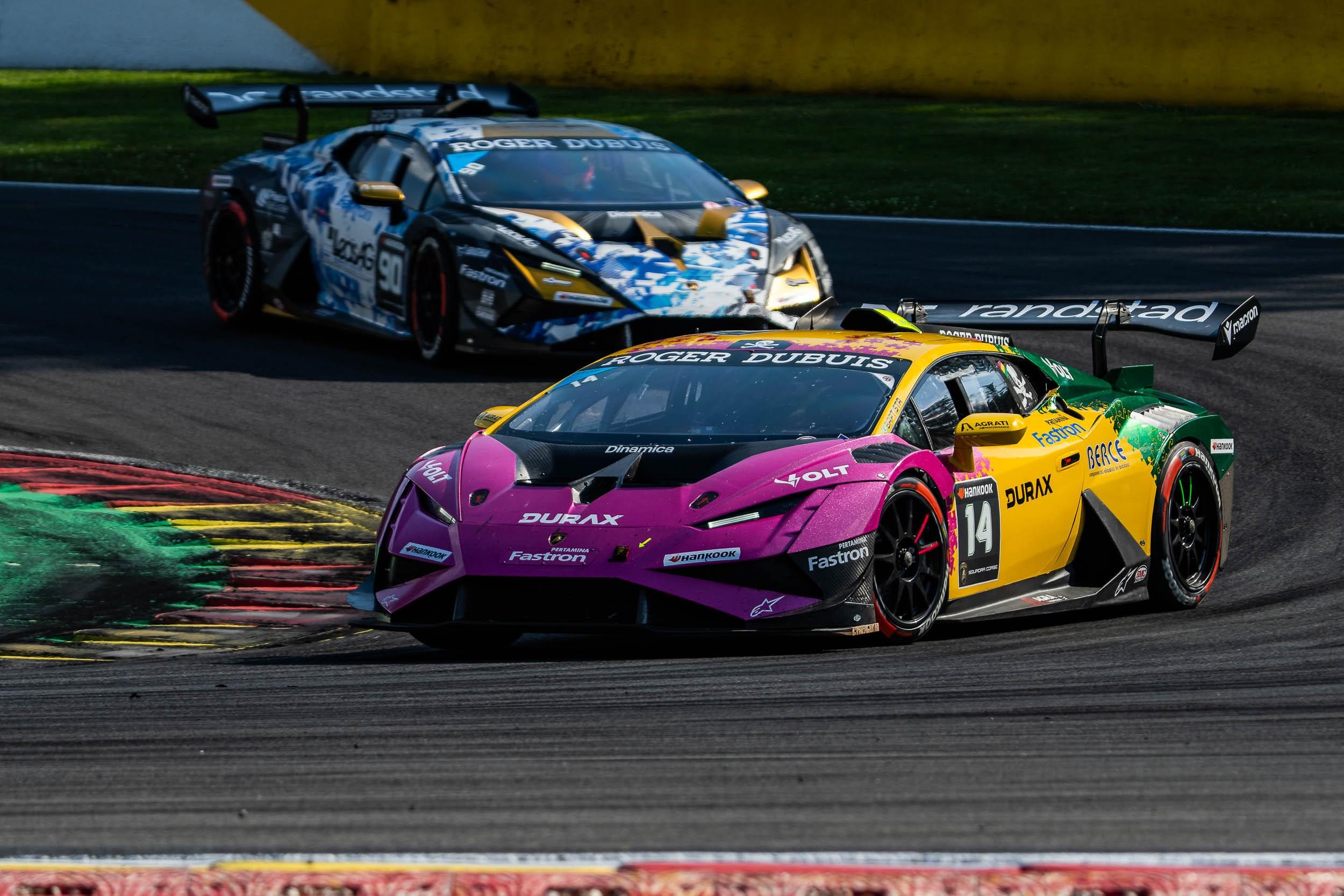 A pink, yellow, and green Lamborghini Huracán Super Trofeo EVO2 race car number 14 leads another car through a racetrack turn