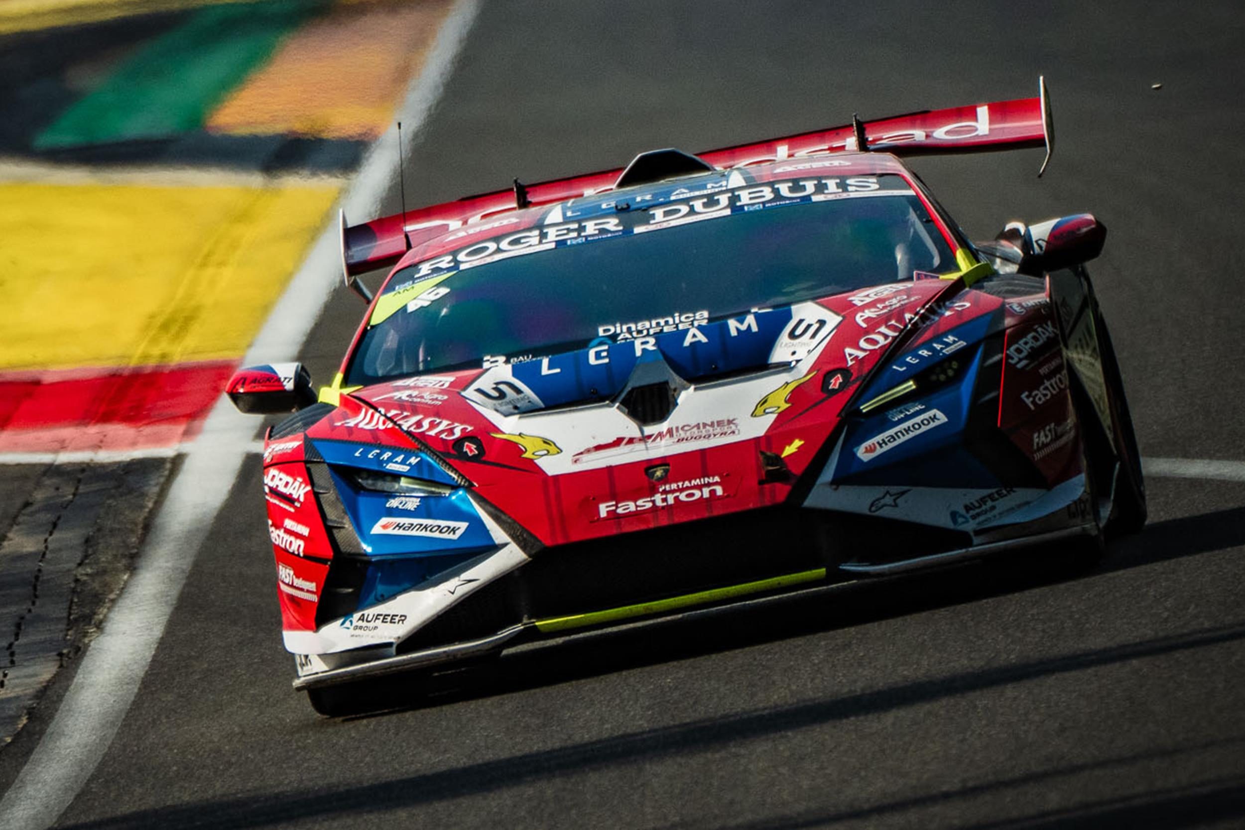 A red, white, and blue Lamborghini Huracán Super Trofeo EVO2 race car, number 11, speeds straight down a racetrack with motion blur.
