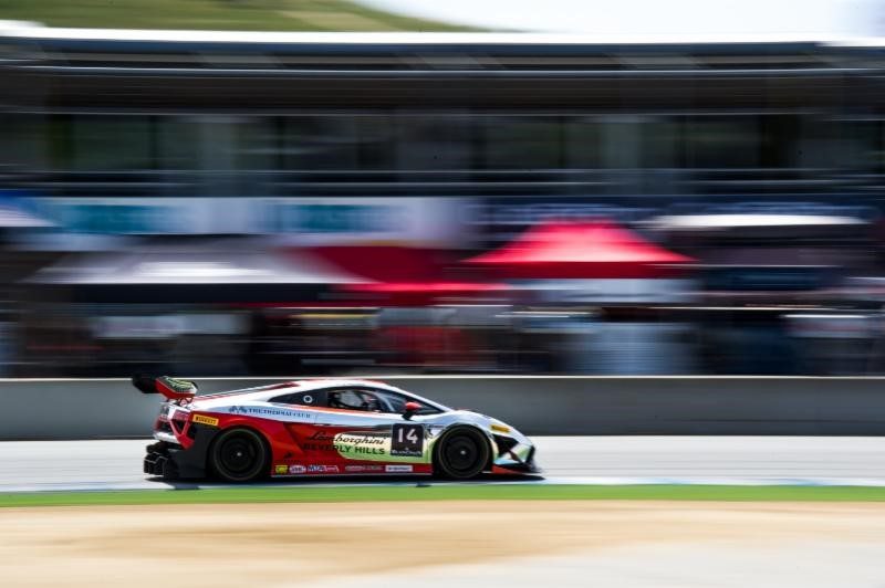 A red and white Lamborghini Gallardo LP 570-4 Super Trofeo race car at speed on a racetrack, captured with motion blur emphasizing the aggressive aero kit and large rear wing