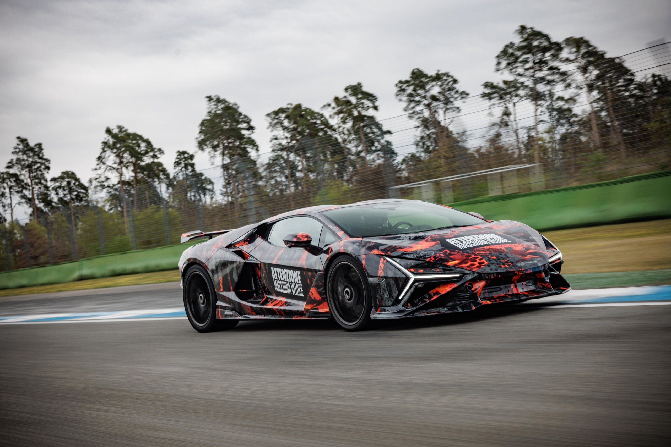 Lamborghini revuelto sv prototype in black and red camouflage at speed on the hockenheimring circuit