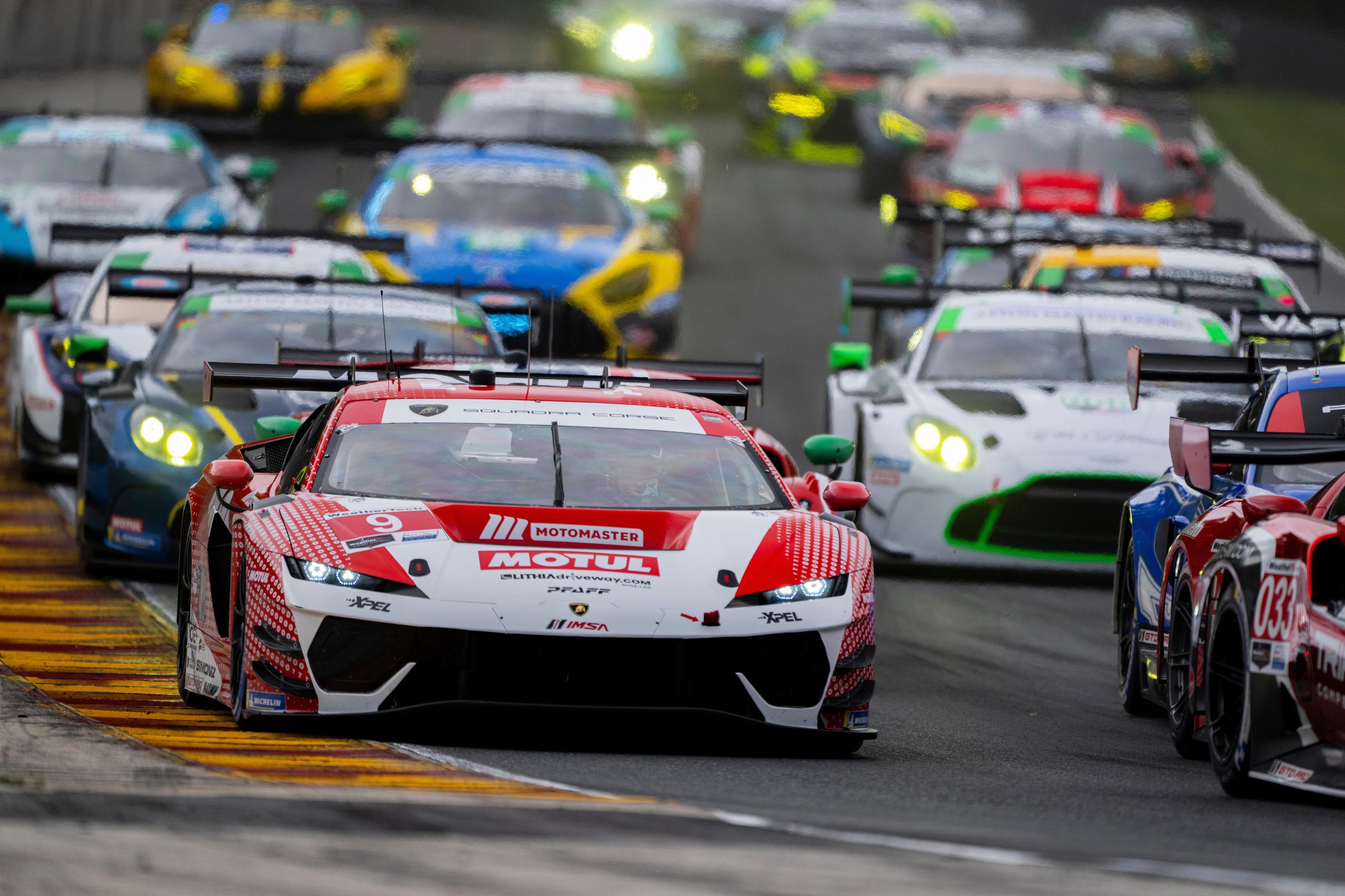 Temerario Gt3 Wins First Imsa Endurance Race At Road America, Five Months After Its Debut 5 The lamborghini temerario gt3 in red and white livery leads a pack of race cars on a wet track, led headlights cutting through spray
