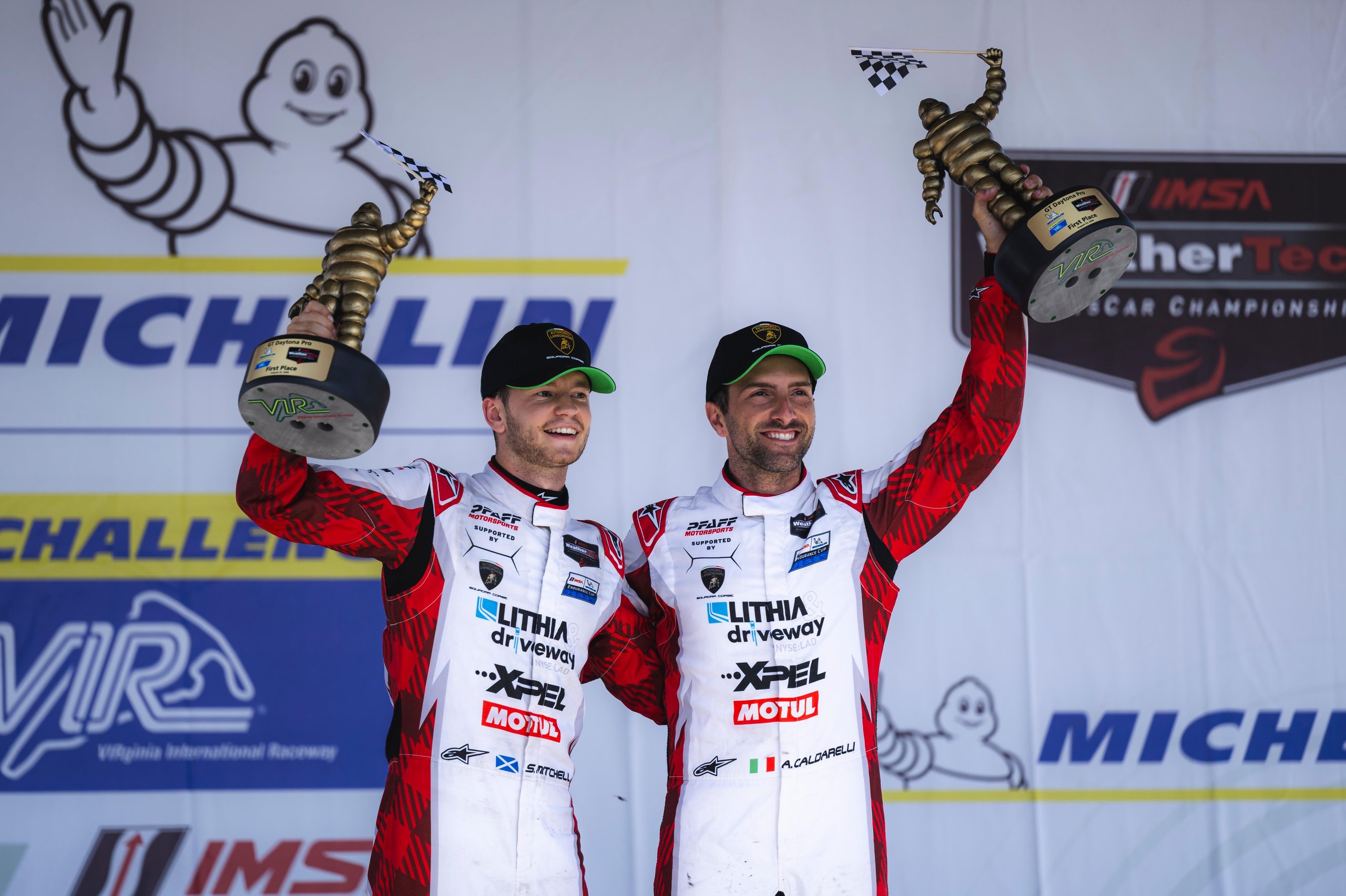 Andrea Caldarelli and Sandy Mitchell celebrating on the podium at VIR with trophies and checkered flags
