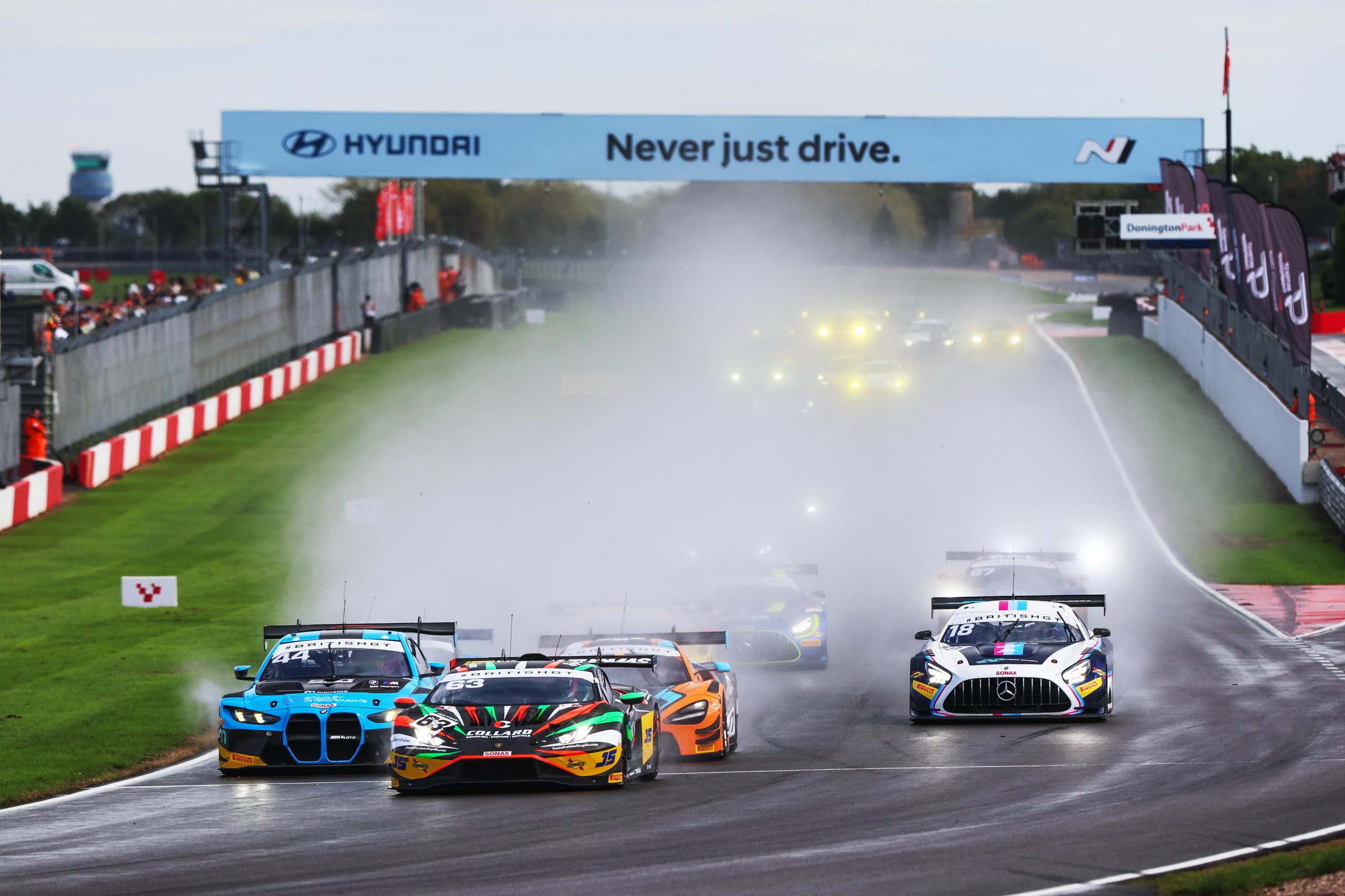 Multiple GT3 race cars including the Lamborghini Huracán GT3 EVO2 kicking up spray on a wet Donington Park circuit
