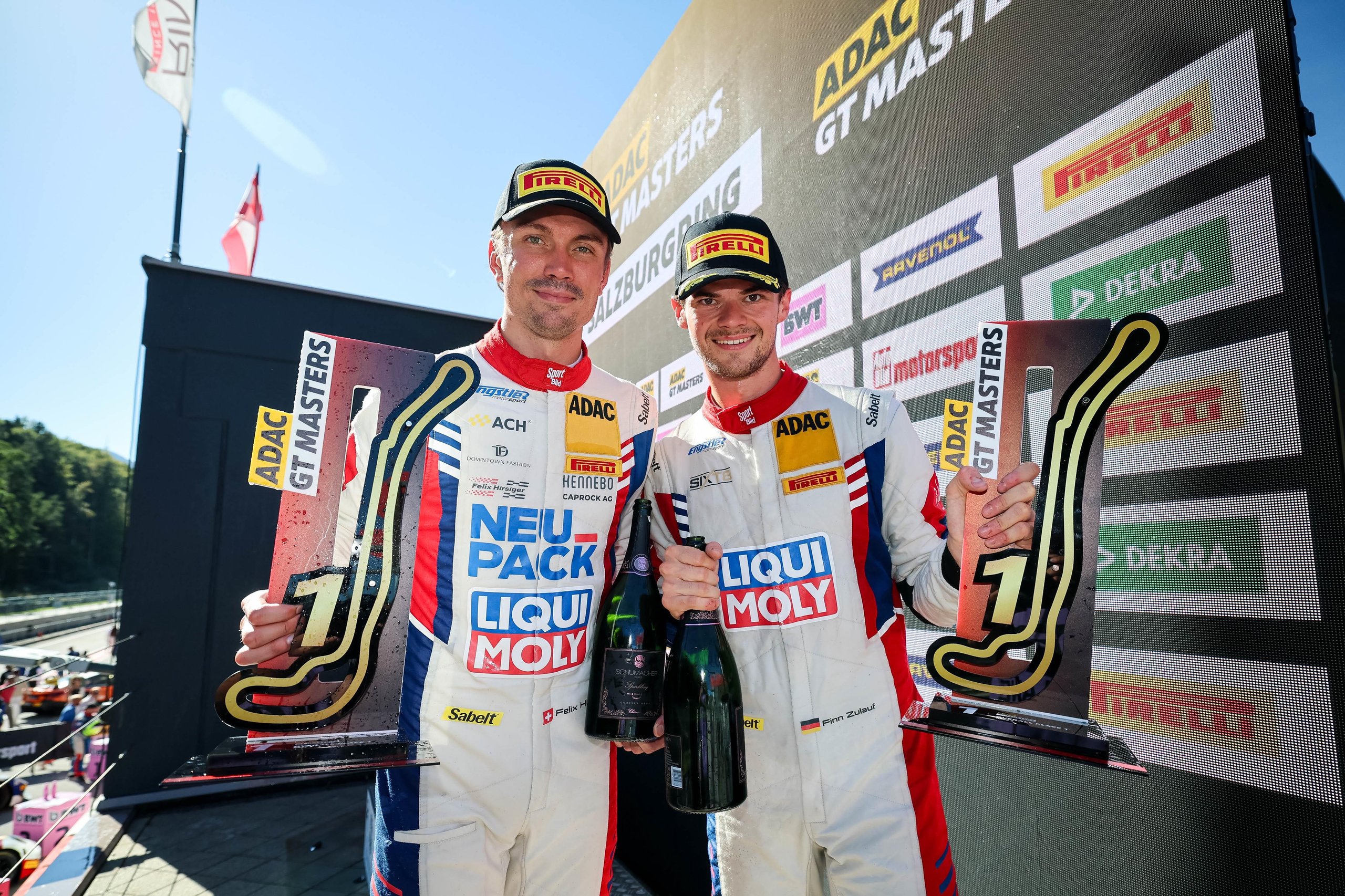 Finn Zulauf and Felix Hirsiger celebrating on the ADAC GT Masters podium with trophies and champagne