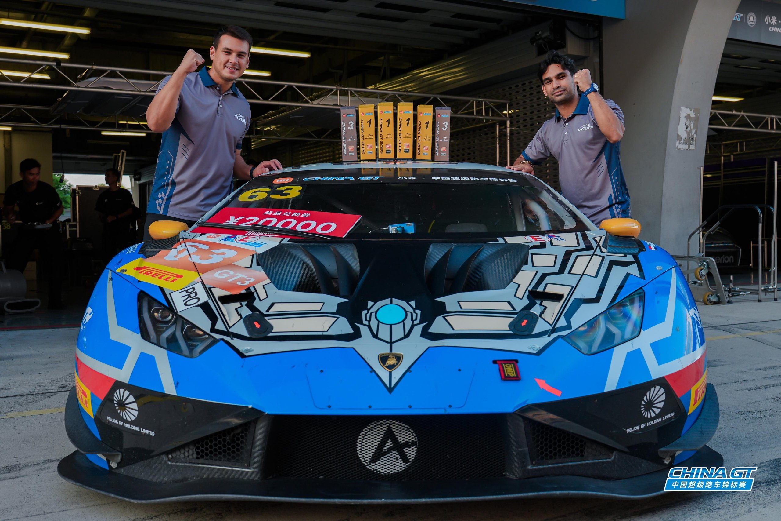 Two team members celebrating with the blue and white Lamborghini Huracán GT3 EVO2 number 63 in the pit lane