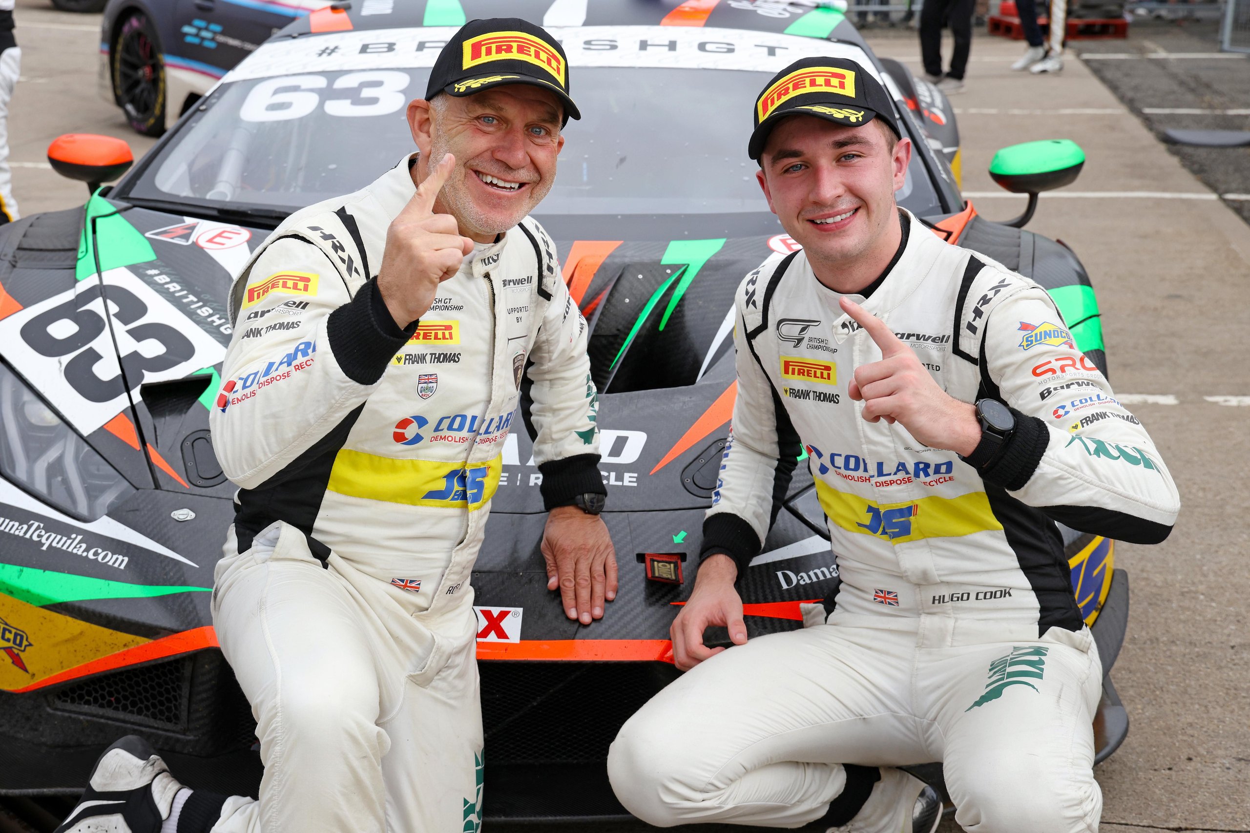 Two male race car drivers pose in front of a multi-colored Lamborghini Huracán GT3 EVO2 race car, number 63, on a racetrack.