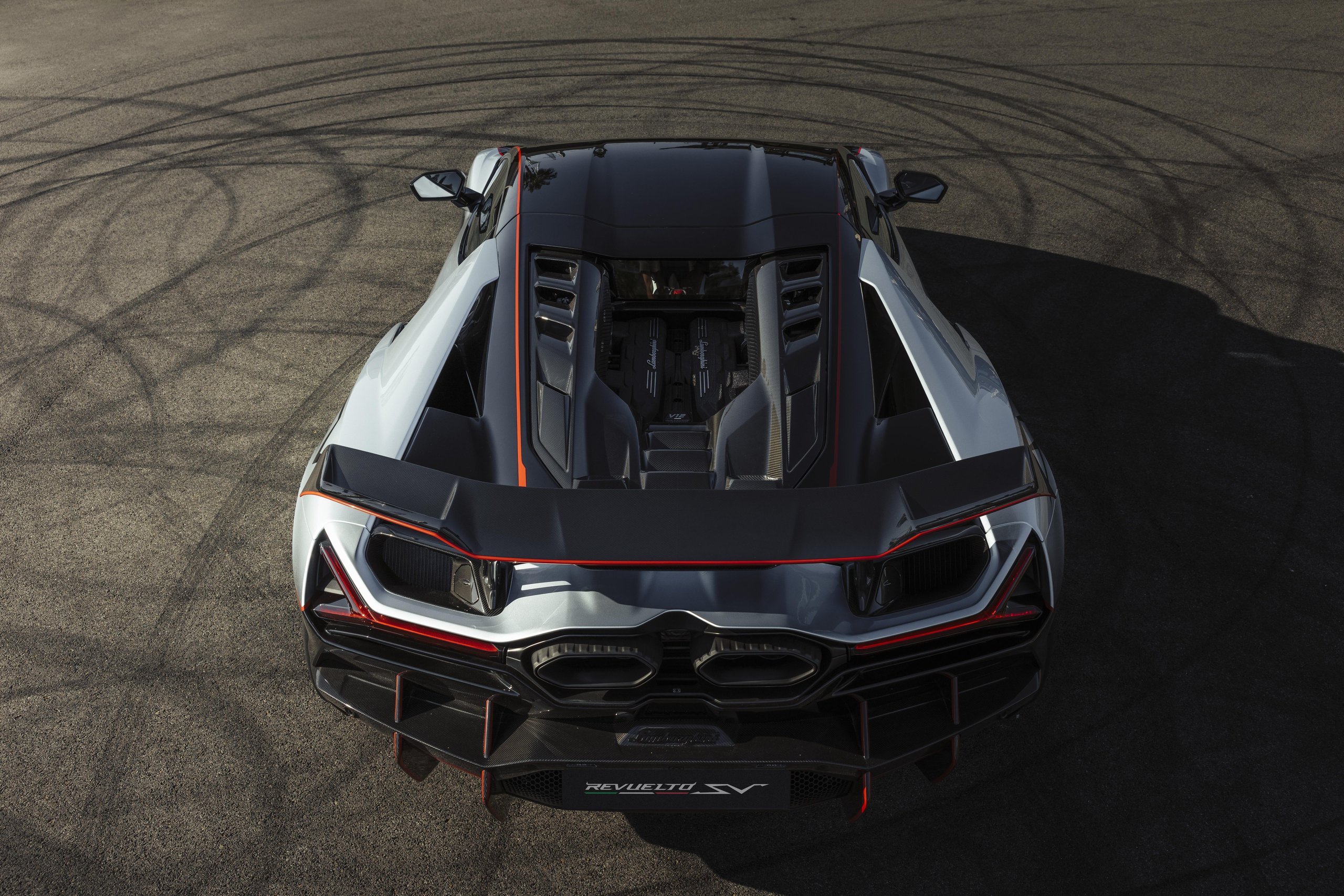 Overhead rear view of grey and black Lamborghini Revuelto SV on track with tire marks, showing exposed engine bay and carbon fiber details