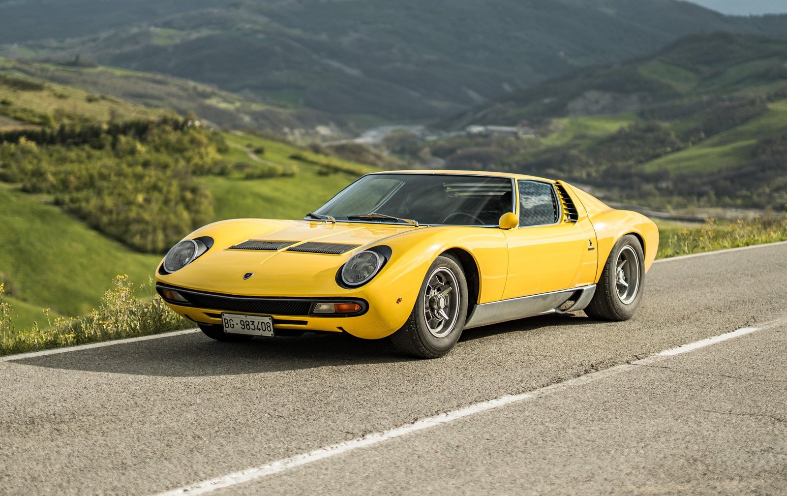 Yellow Lamborghini Miura SV on a winding mountain road, the car that started the Super Veloce lineage in 1971